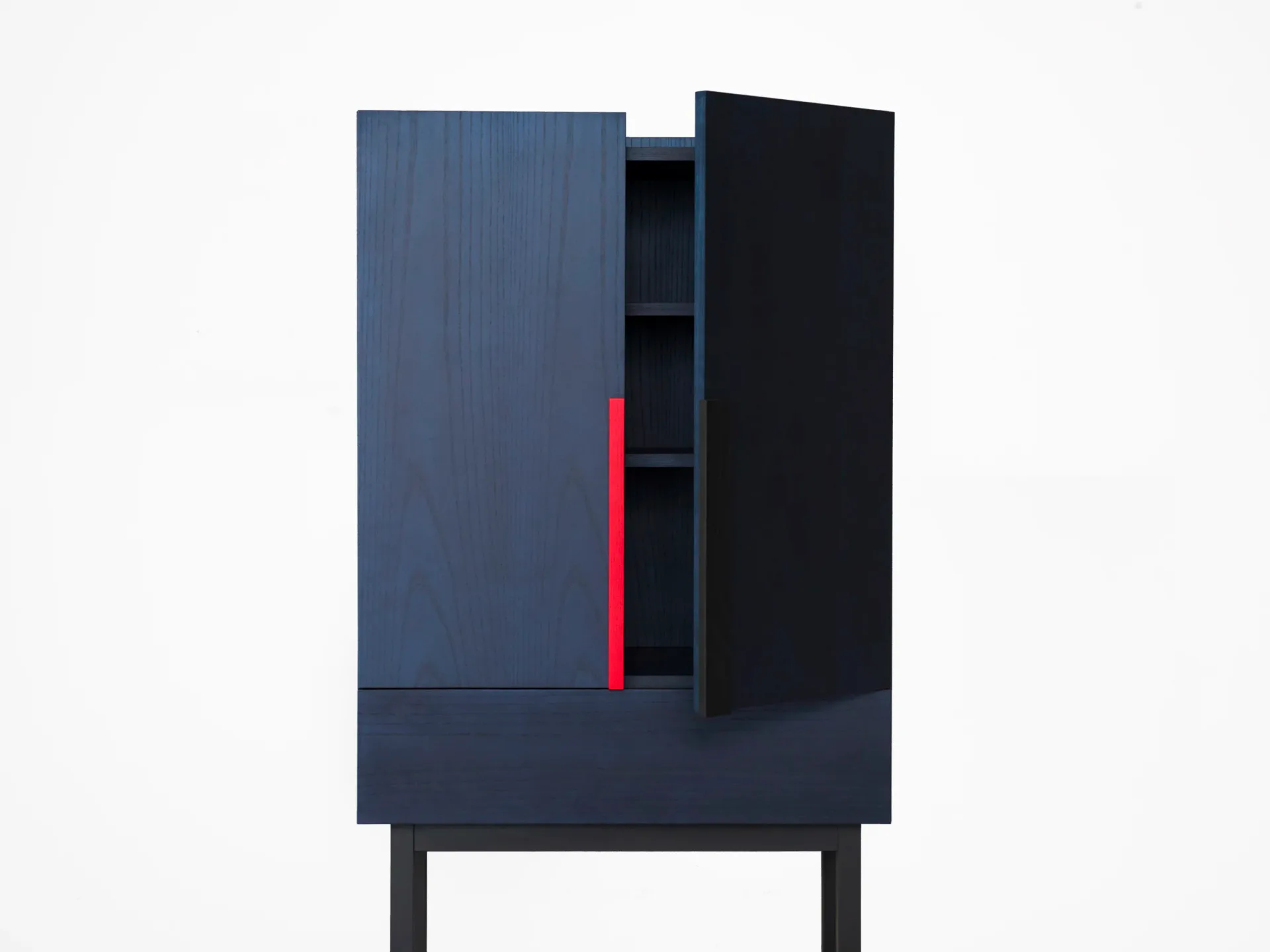 Dark navy cabinet with open shelving and a striking red vertical element, mounted on black legs, designed by Zoë Mowat.