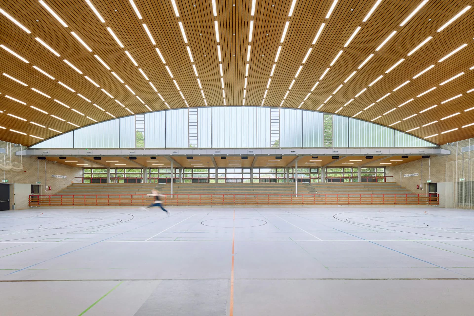 A spacious modern gymnasium with arched timber ceiling, expansive glazing, polished flooring, and natural light by 1100 Architect.