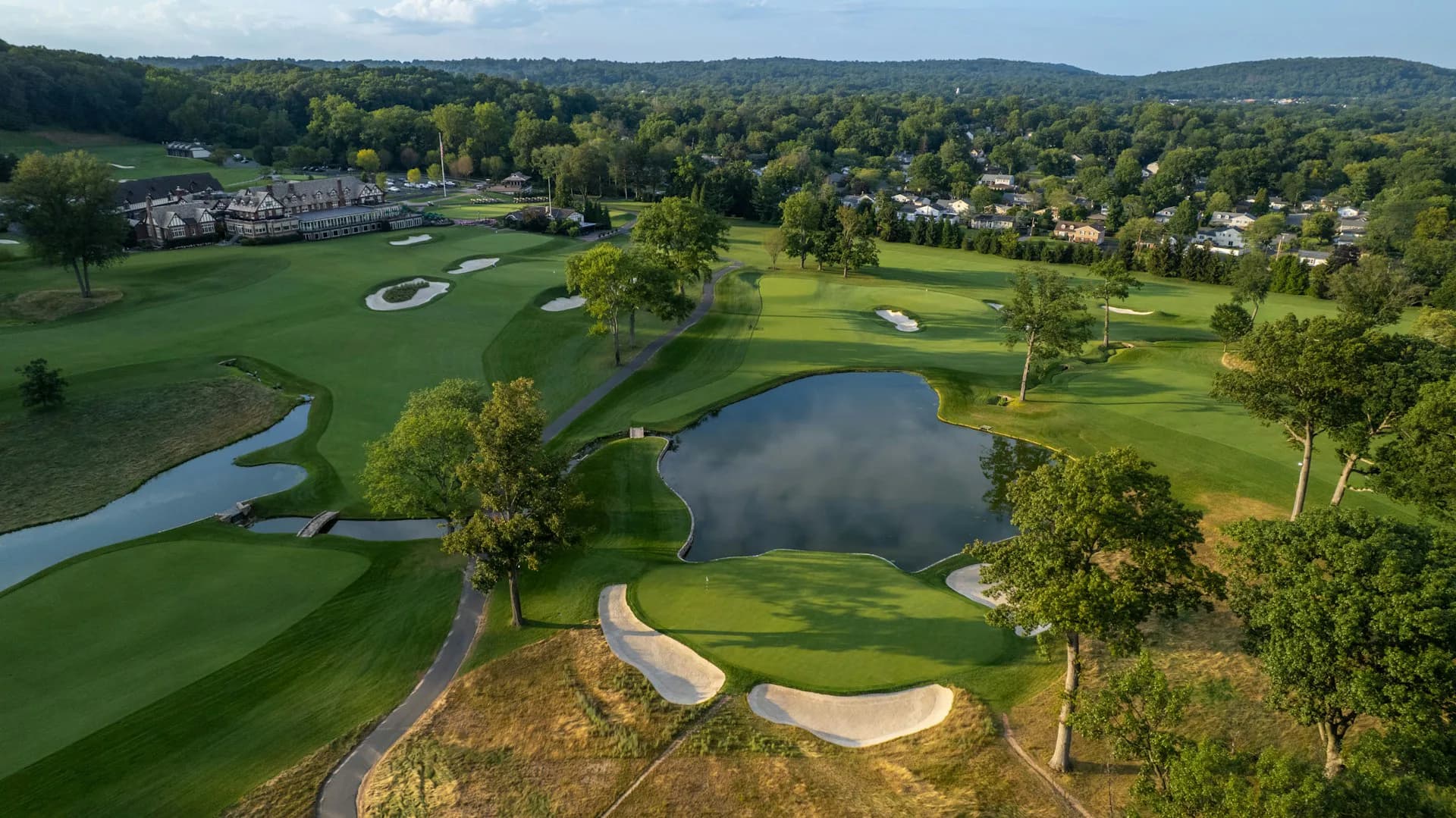 Aerial view of a golf course design featuring manicured fairways, water features, sand bunkers, and mature trees integrated throughout the landscape by 1100 Architect.