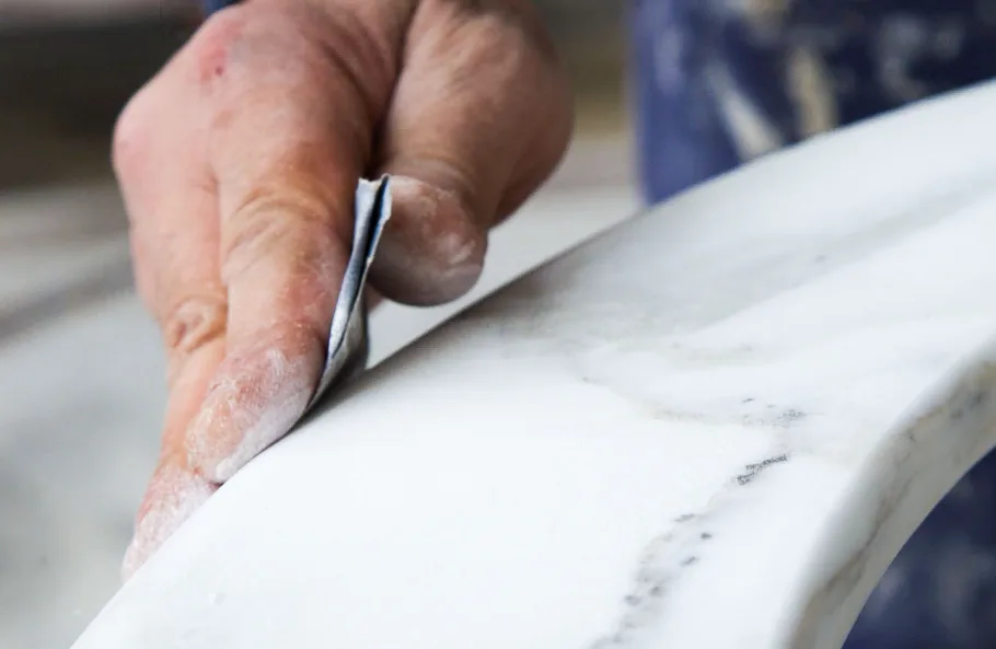 Close-up of a craftsman's hand using a chisel on white marble, demonstrating stone finishing techniques by 29 Street Stone Inc.