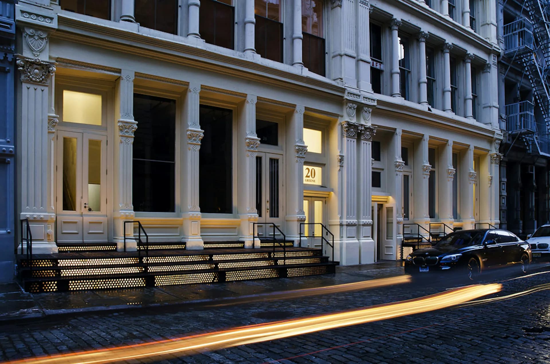 Classical facade with tall fluted columns, illuminated storefront entrances, and golden hour lighting casting long shadows across a brick plaza by AC Hocek Architecture LLC - (ACHA).