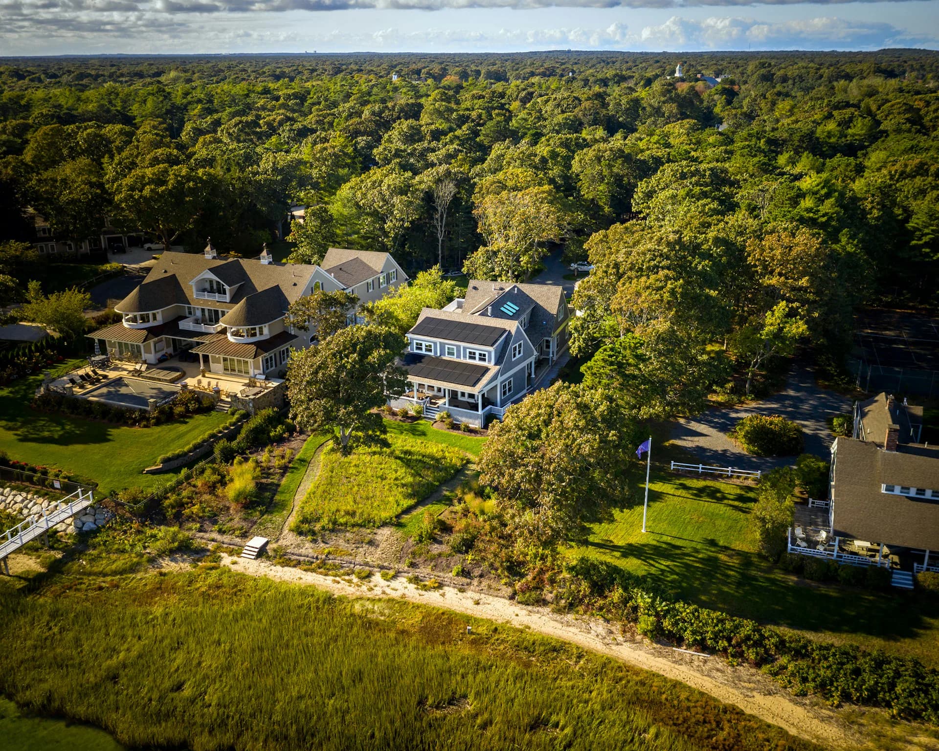 Aerial view of residential waterfront properties nestled among mature trees with manicured lawns and beach access, designed by Acheson Doyle Partners Architects, P.C.