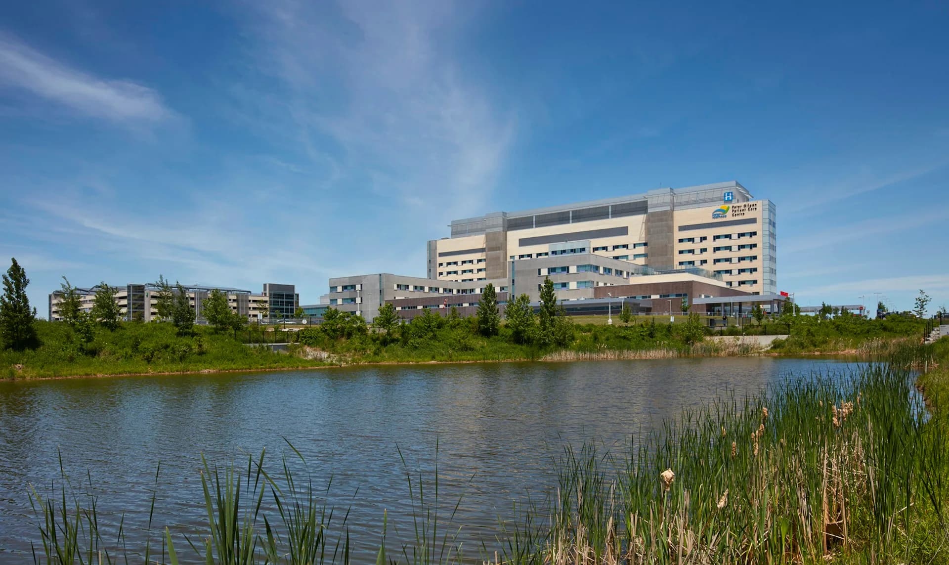 Modern multi-story hospital building with horizontal banding overlooking a naturalistic wetland pond with native vegetation by Adamson Associates Architects.