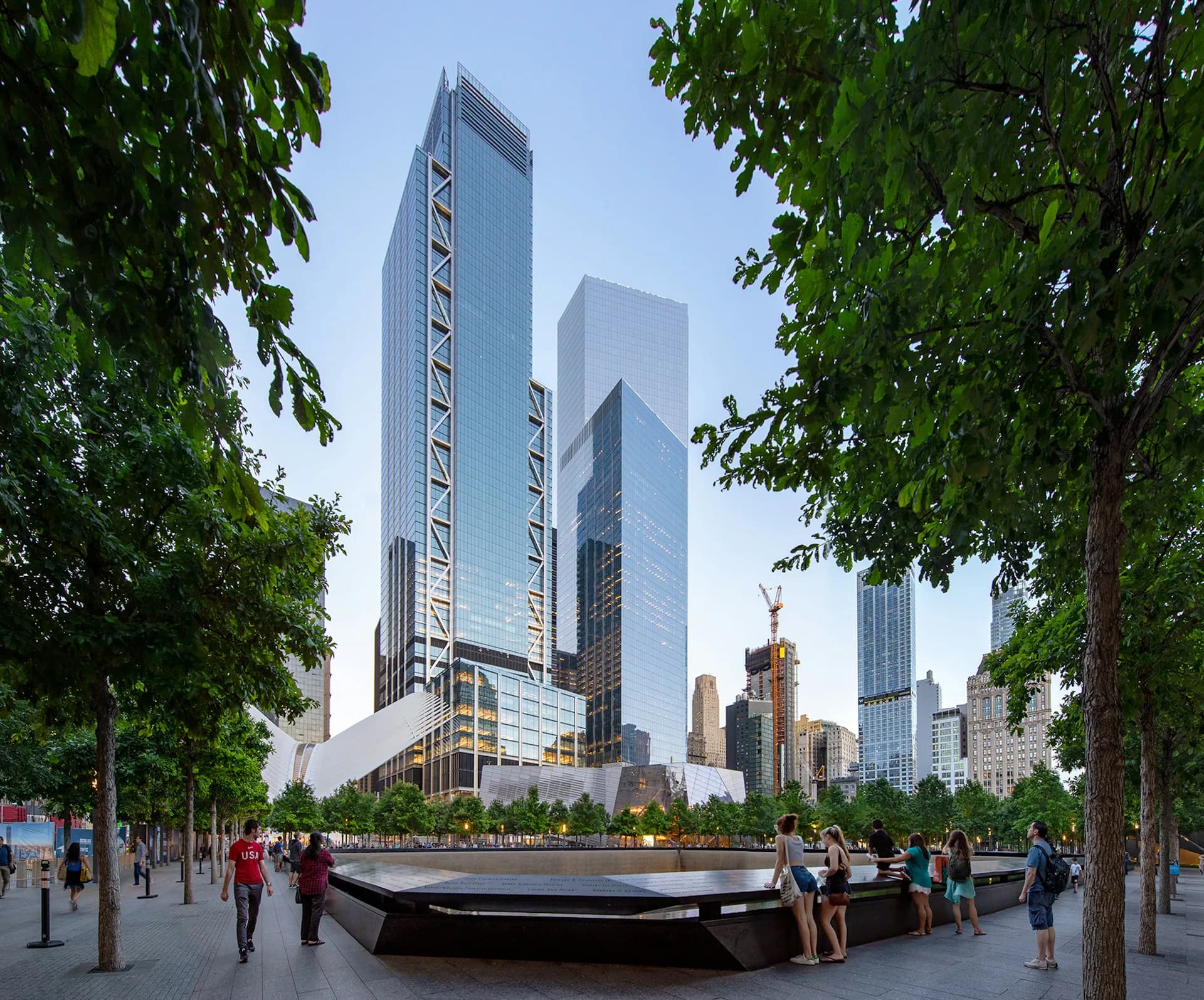 Architectural rendering of modern glass and steel towers in an urban plaza with green trees framing the view, featuring a sculptural water feature and pedestrians, by Adamson Associates Architects.