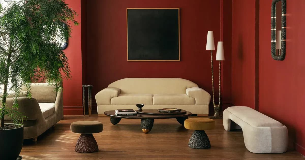 Modern living room with curved cream sofa, red walls, wooden flooring, potted plant, black coffee table, and contemporary accessories designed by Aguirre Design.