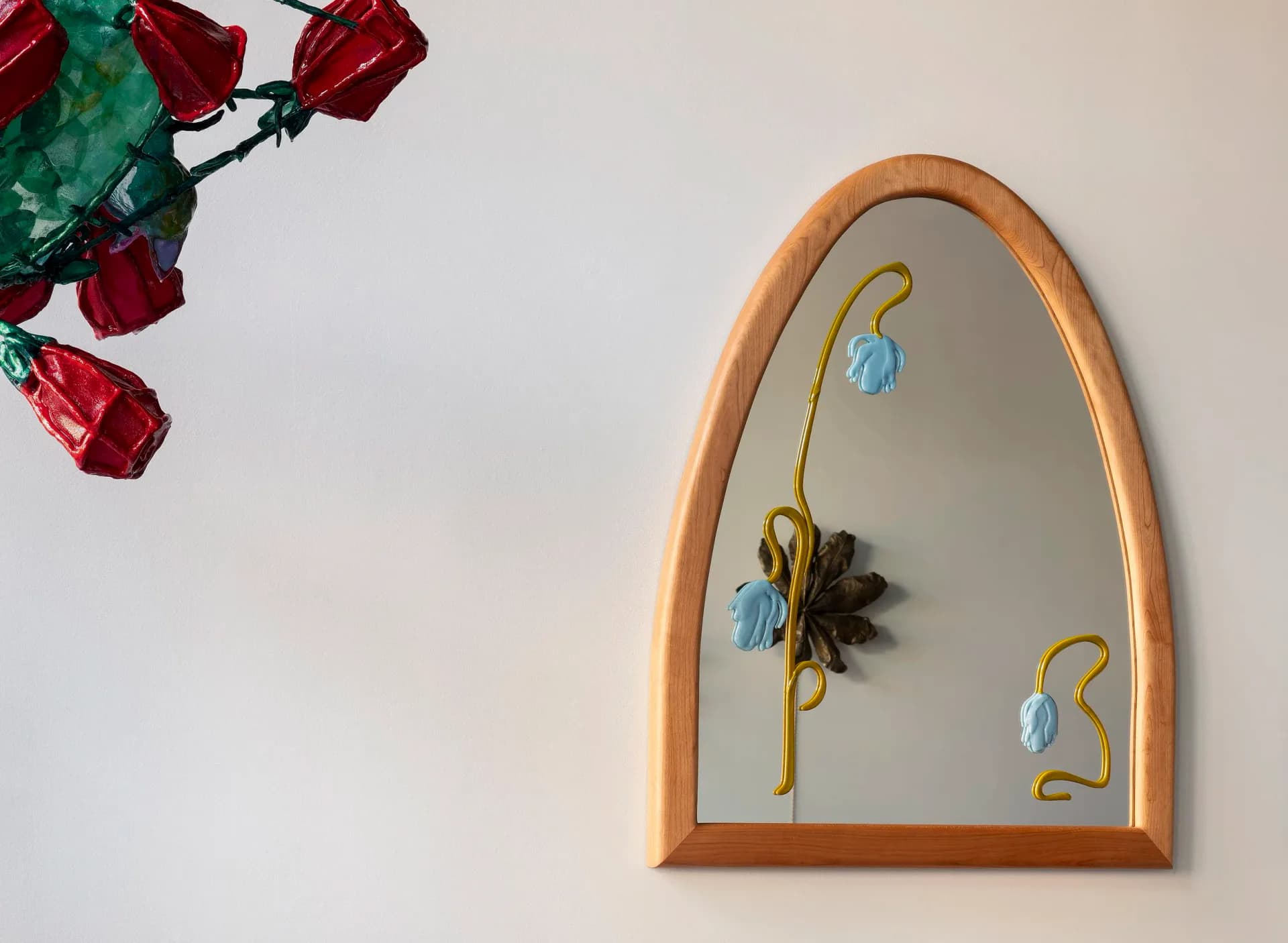 Arched wooden mirror with painted botanical details featuring delicate blue flowers and green stems against a white wall by Alexis & Ginger.