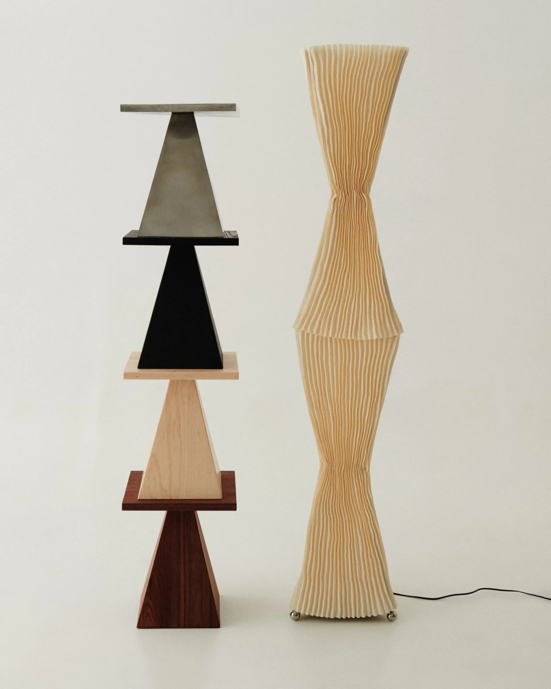 Two sculptural lighting installations featuring stacked geometric forms—one with alternating metal and wood trapezoid shapes, the other a fluted wooden hourglass silhouette by Alexis & Ginger.