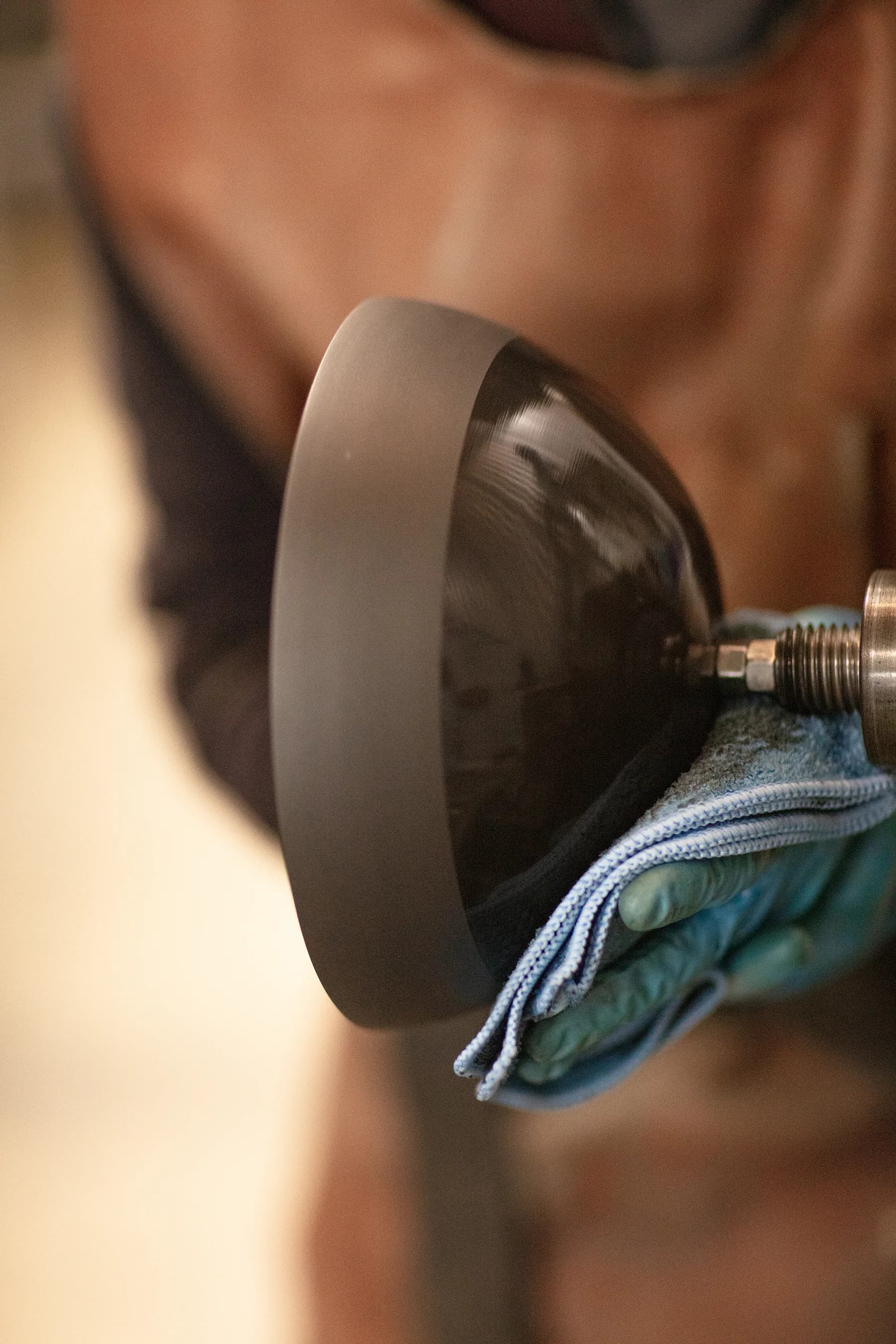 Close-up of a spherical dark pendant light fixture with matte gray collar and metal fixture, held in hands against blurred background by Allied Maker.
