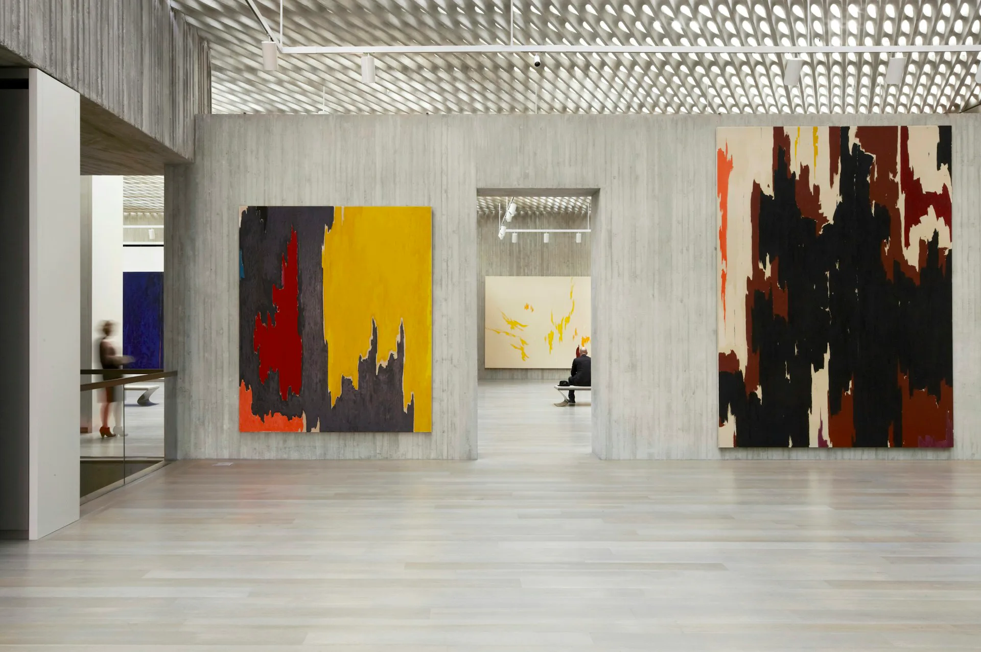 Modern gallery space with polished concrete floors, white walls, and geometric patterned ceiling displaying large abstract paintings in bold colors by Allied Works.