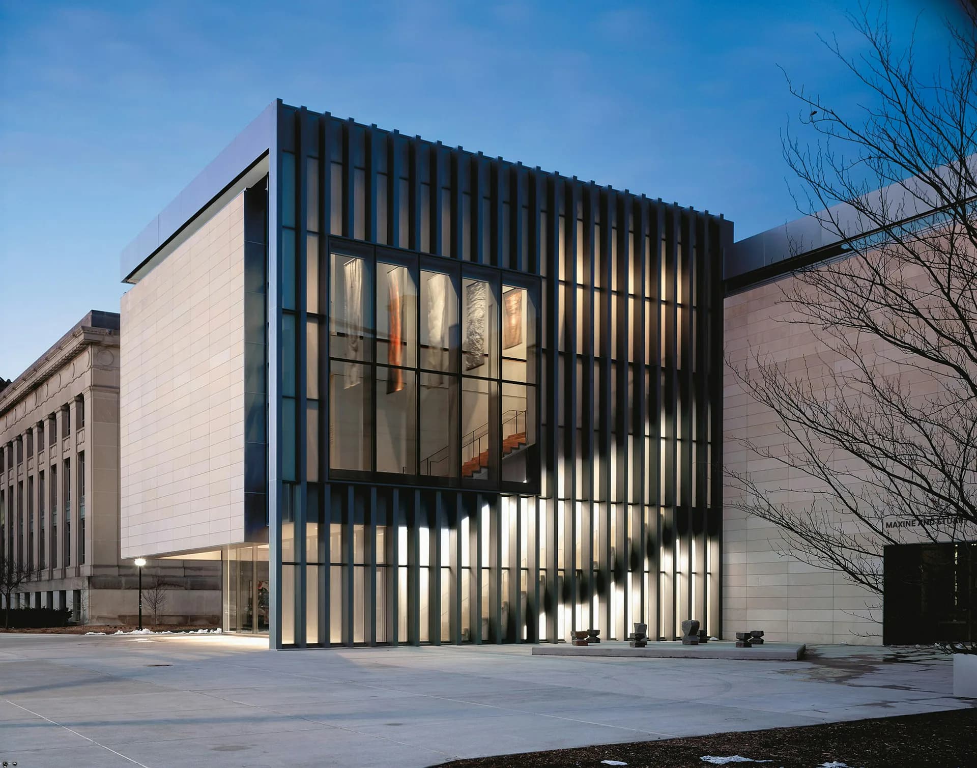 Modern institutional building with white brick facade and prominent black vertical-slat screen element, minimalist courtyard setting by Allied Works.