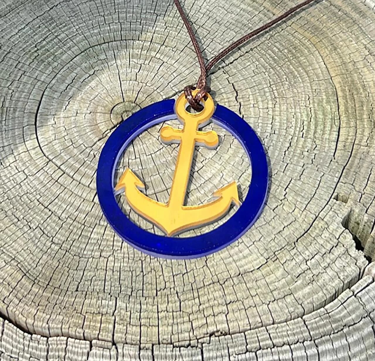Yellow anchor pendant with blue circular frame hung from a branch against textured wood background, by Allison Eden Studios.