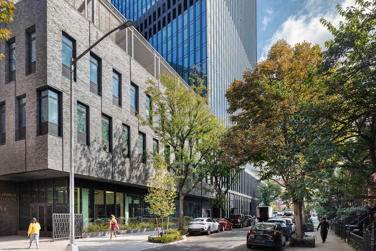 Street-level rendering of mixed-use urban development with stone facade building, ground-floor retail, trees, and modern tower backdrop by Alloy Development.