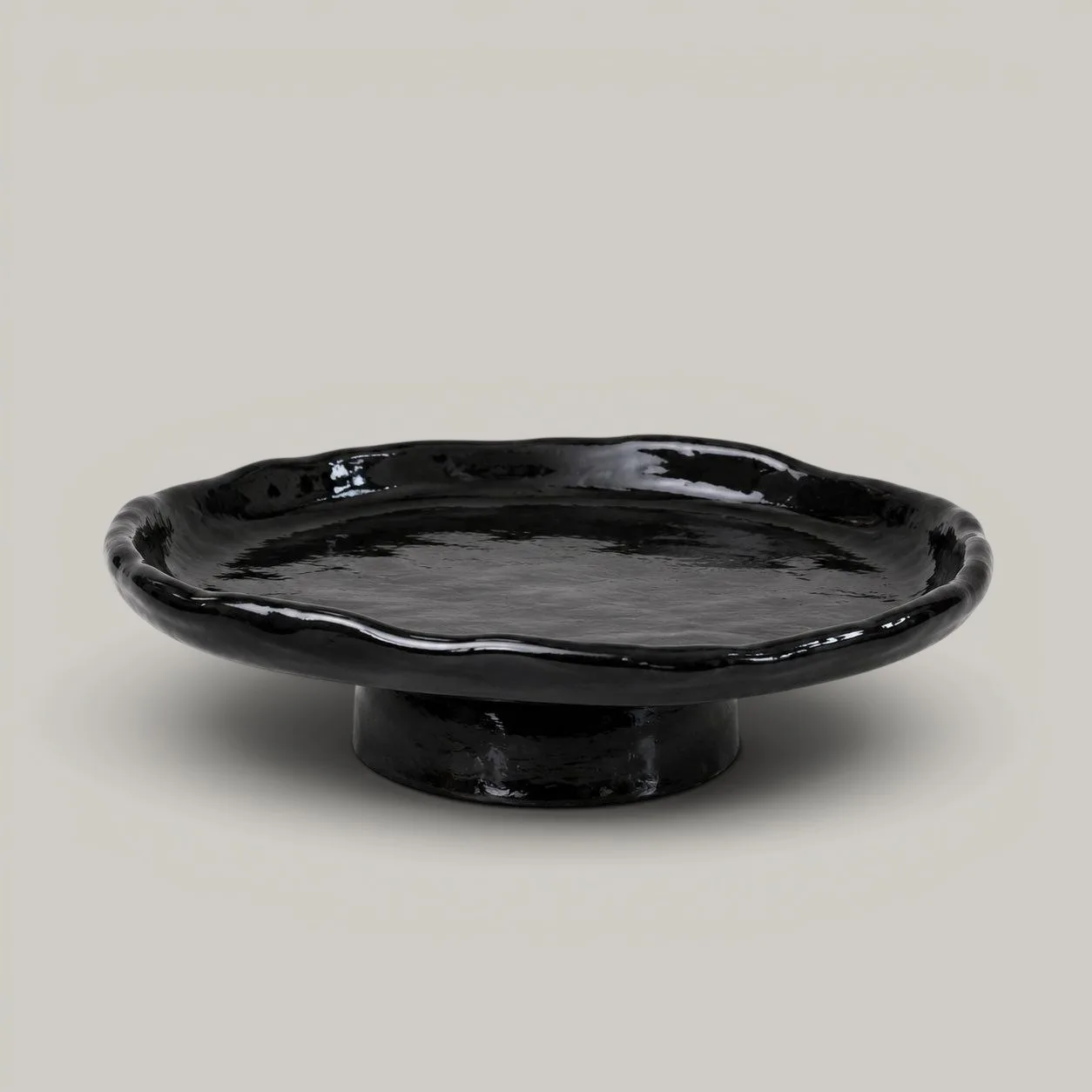 Black glazed ceramic pedestal bowl with organic rim detailing and subtle surface variations by Alter Ego Studio.