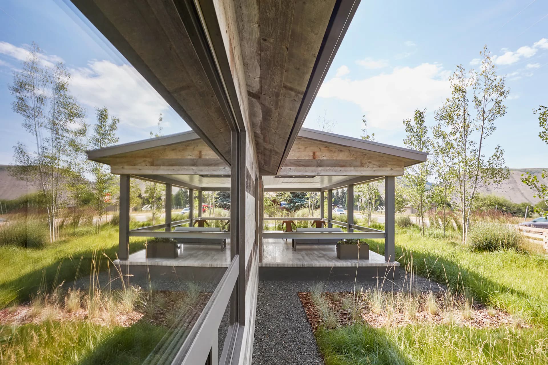 Modern pavilion structure with wooden roof and concrete walkway surrounded by native grasses and trees by AMMOR Architecture LLP.