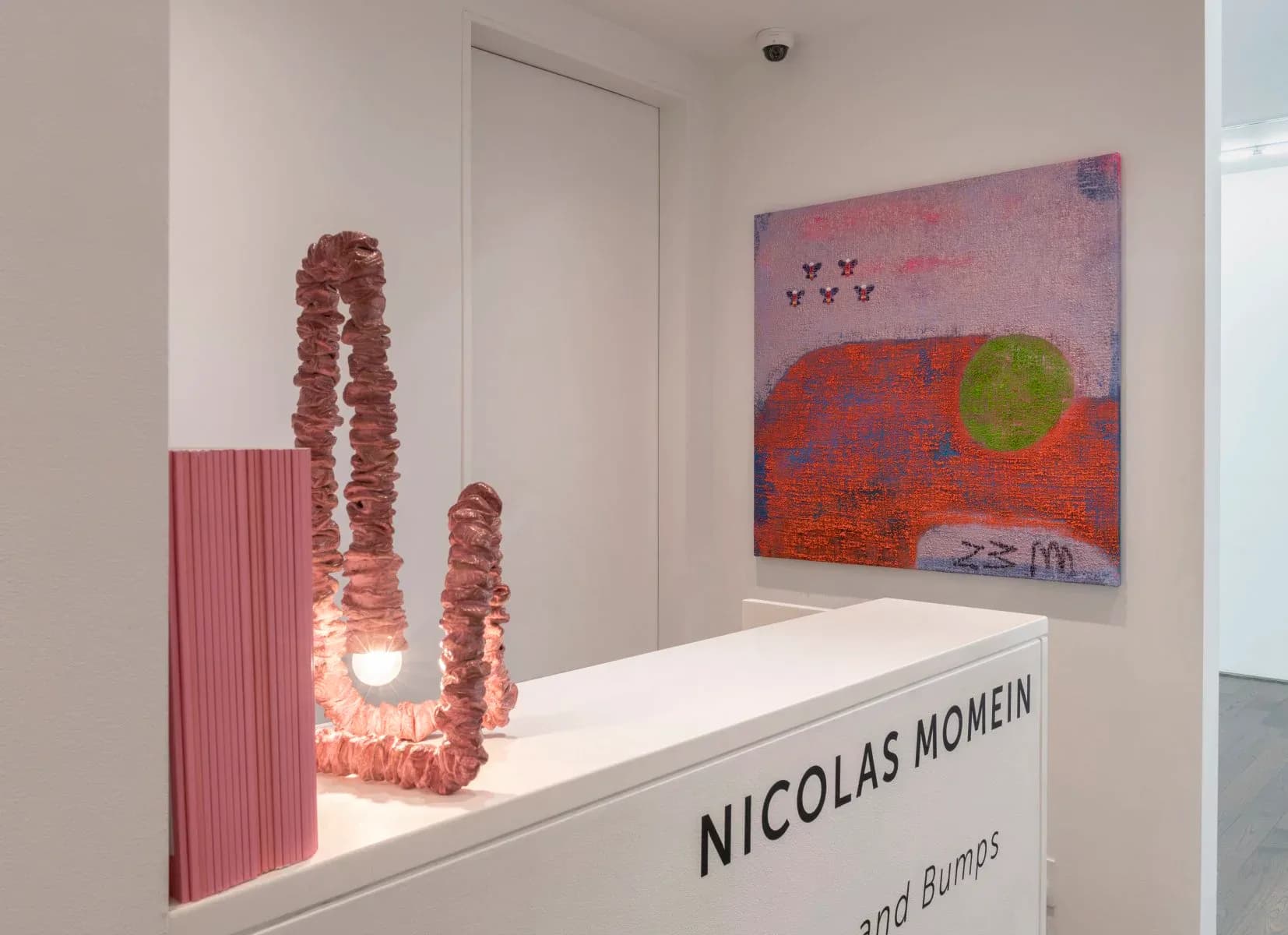 Modern gallery space with white walls displaying contemporary art and sculptural installations, featuring coral-toned ceramic pieces and colorful abstract painting by Ampersand Architecture.