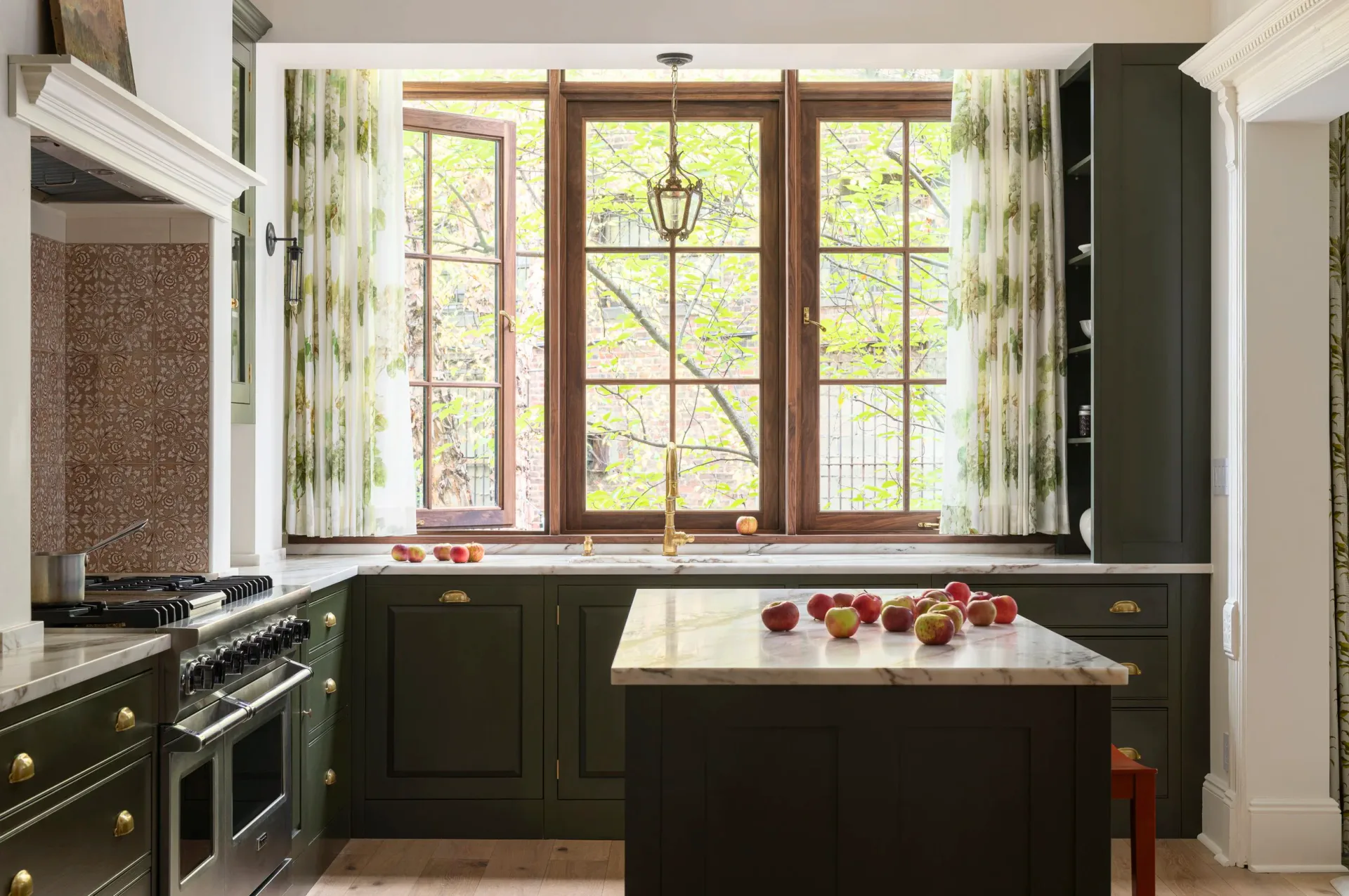 A contemporary kitchen with dark cabinetry, marble countertop, and large multi-pane windows overlooking greenery, designed by Anat Soudry Architect.