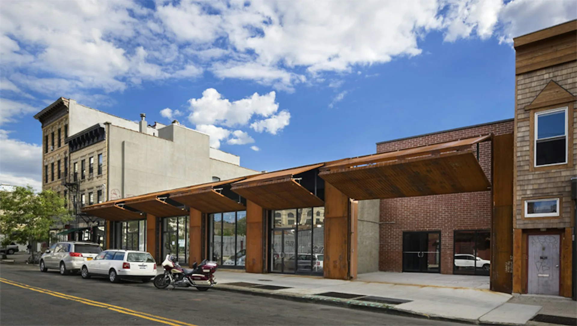 Street-front renovation with warm wood and brick materials, glass storefront, and covered wooden canopy addition by Andre Kikoski Architect.