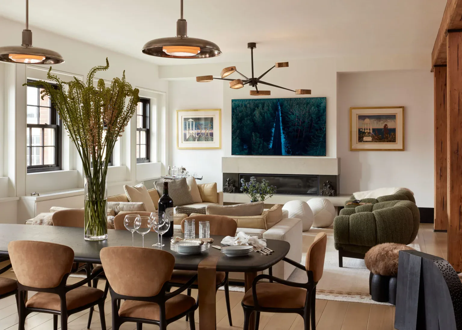 Open-plan dining and living area with warm wood tones, cream upholstery, round dining table with curved chairs, pendant lighting, fireplace with TV, and decorative greenery by Andrew B. Ballard, AIA Architecture & Interior Design.