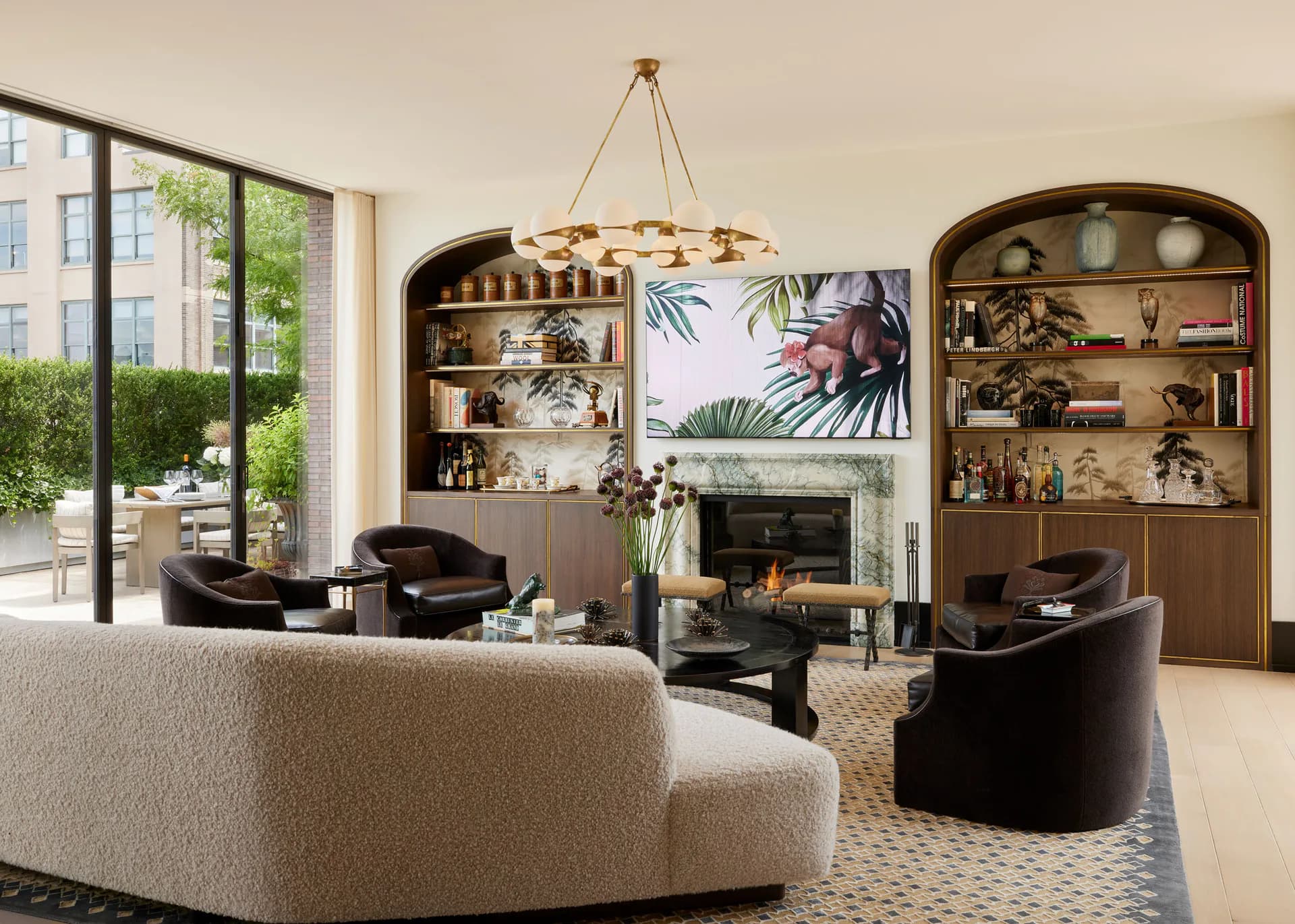 Luxurious living room with curved cream sofa, black accent chairs, arched built-in shelving, fireplace with botanical artwork, geometric patterned rug, and pendant chandelier by Andrew B. Ballard, AIA Architecture & Interior Design.