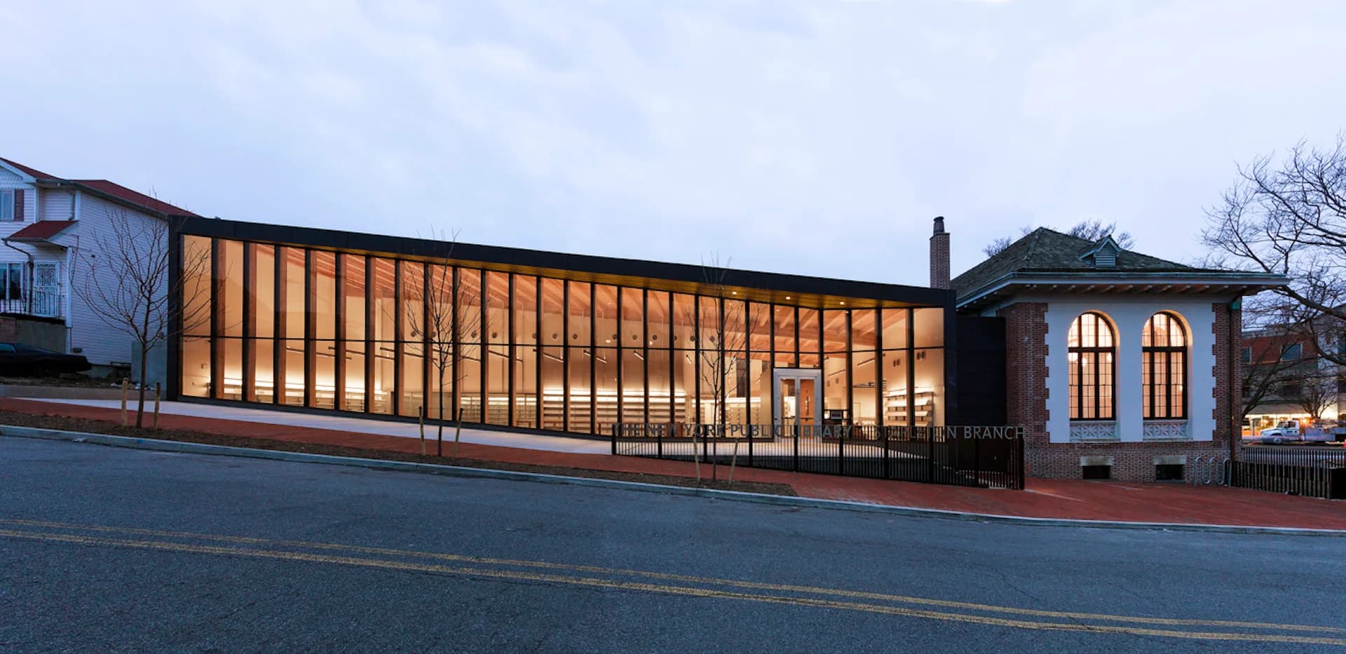Evening exterior of a modern brick extension with warm-lit horizontal wood slats alongside a historic brick building, designed by Andrew Berman Architect.