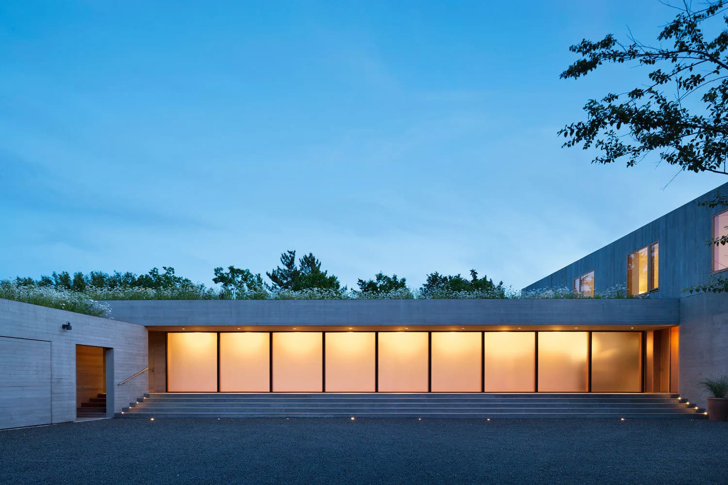 Modern minimalist building with illuminated glass storefront and clean geometric lines at dusk by Andrew Berman Architect.