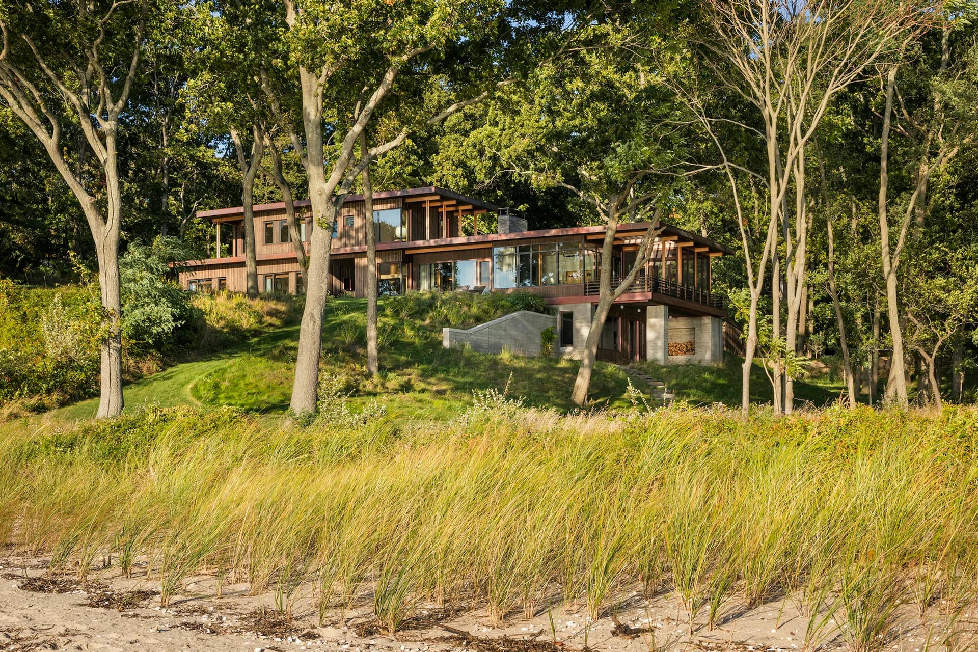 Modern multi-level residential structure with wood and metal cladding nestled among tall trees on a sandy beach landscape by Andrew Franz Architect PLLC.