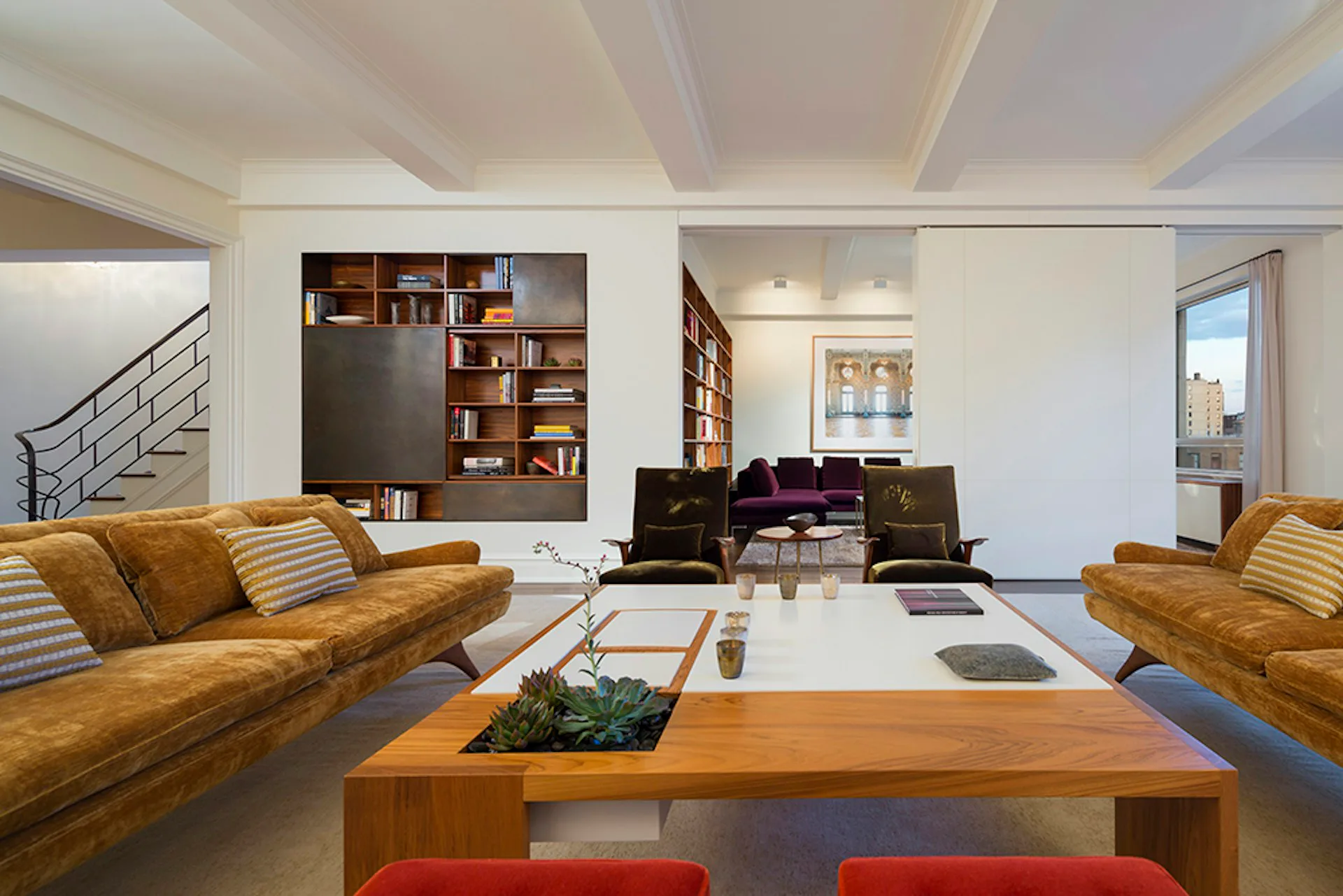 Contemporary loft living room with ochre velvet sofas, wooden coffee table, built-in shelving, and mezzanine level, designed by Andrew Franz Architect PLLC.