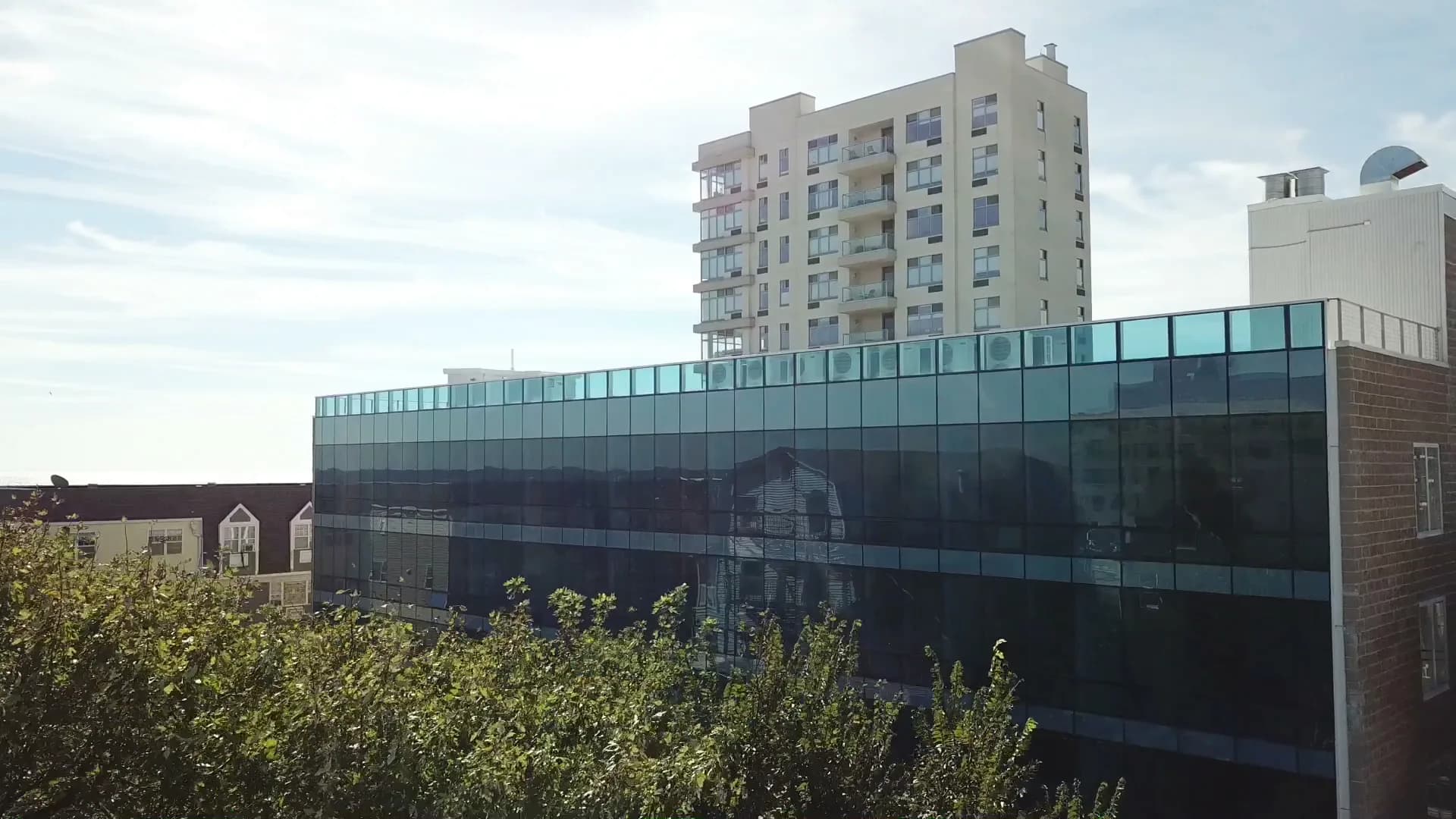 Modern residential building with glass-fronted commercial base featuring dark translucent panels, brick detailing, and apartment tower above by Andrew L. Pettit Architect.