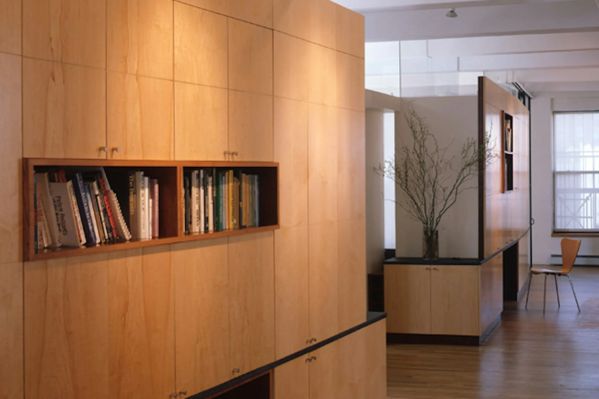 Modern residential interior with warm wood cabinetry, built-in bookshelves, and minimalist furnishings throughout open-plan living space by Ann Marie Baranowski Architect PLLC (AMBA).