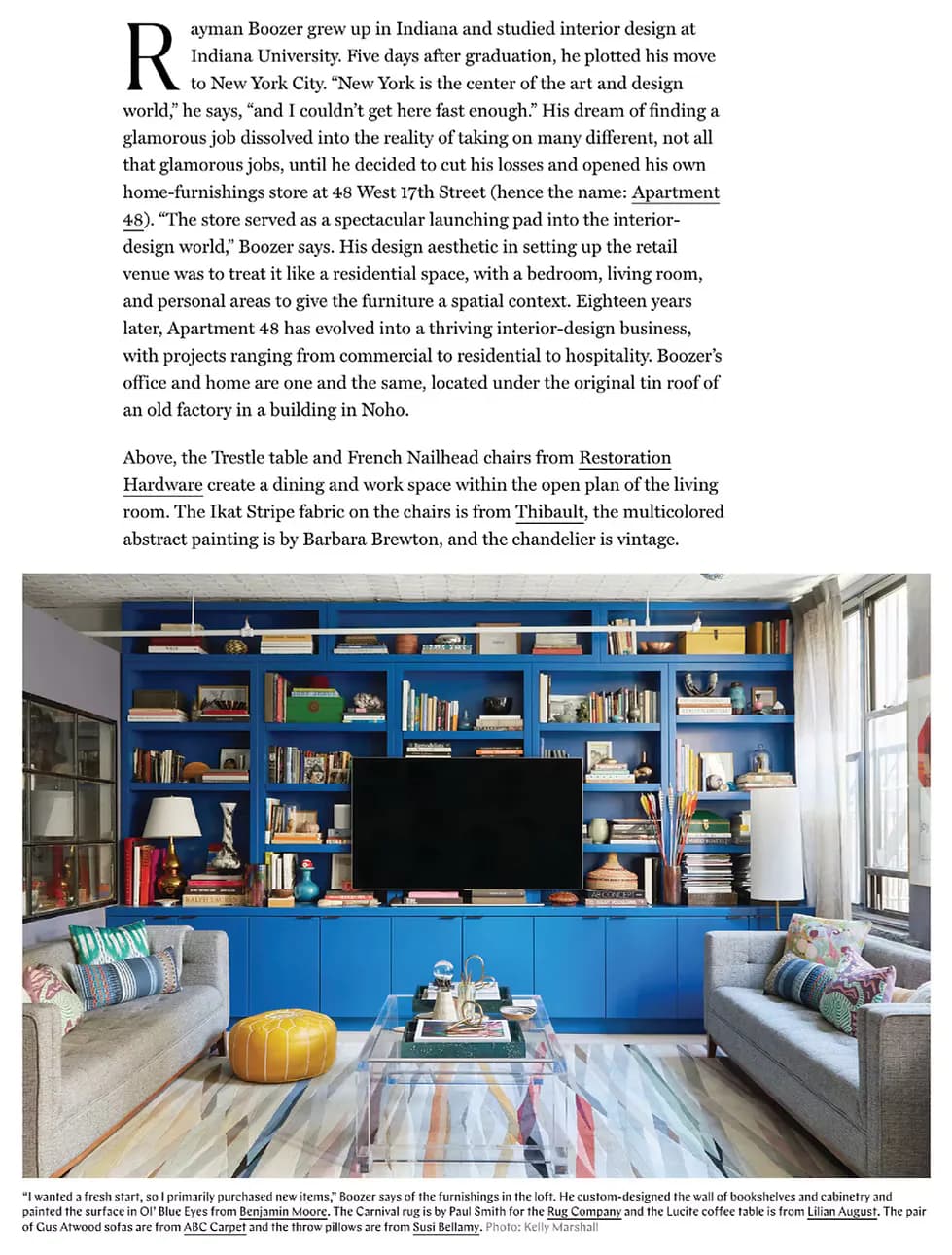A living room with built-in blue shelving, two gray upholstered seating areas, and colorful abstract artwork on the floor by Apartment 48.