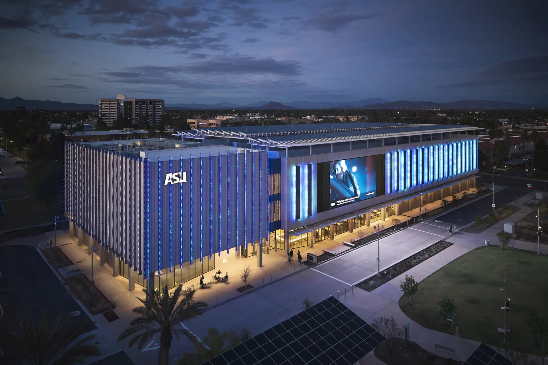 Modern blue architectural building with illuminated vertical striping and signage, photographed at dusk by Apeiro Design.
