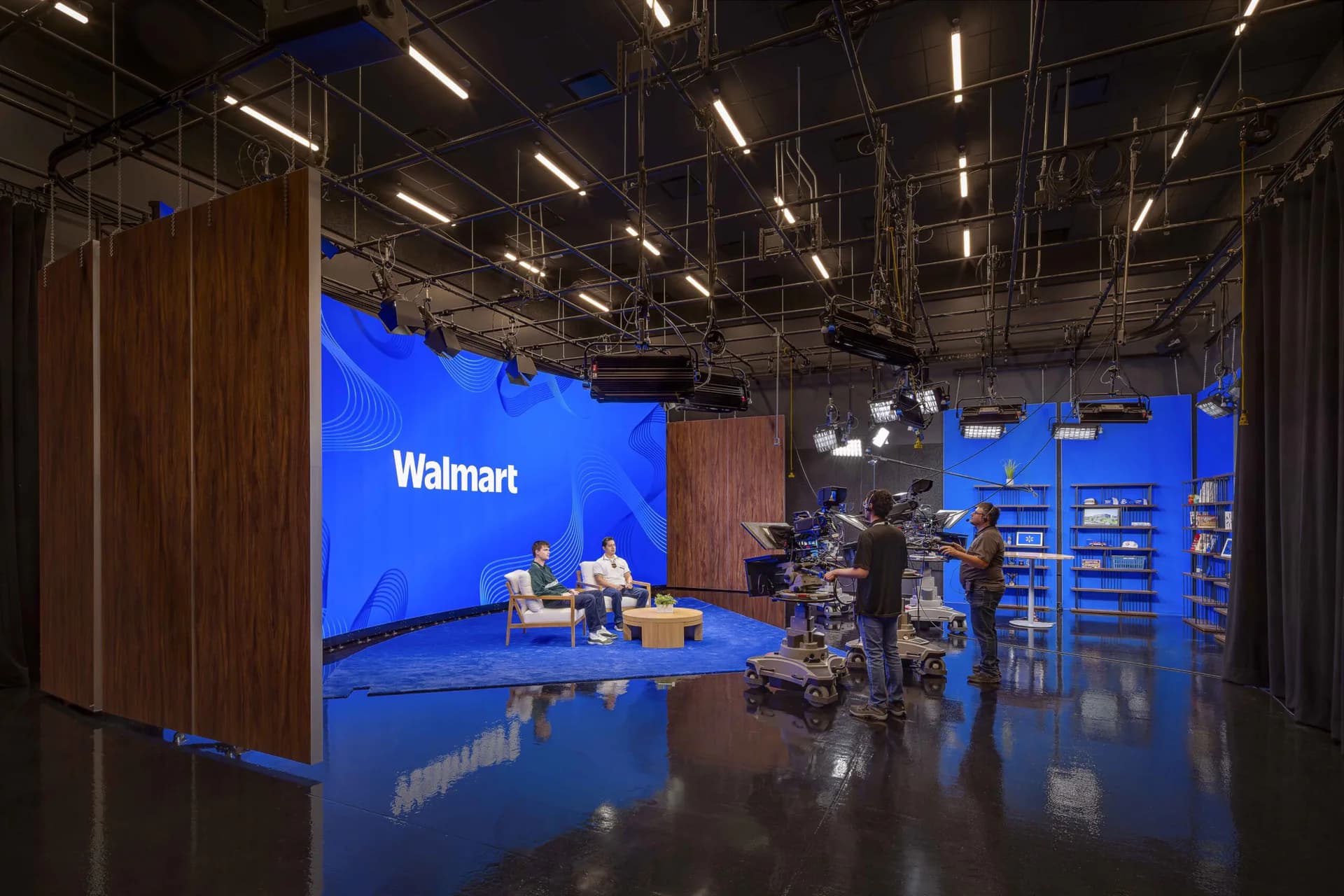 Modern broadcast studio with blue accent walls, wooden paneling, and professional lighting, featuring a Walmart-branded presentation stage by Apeiro Design.