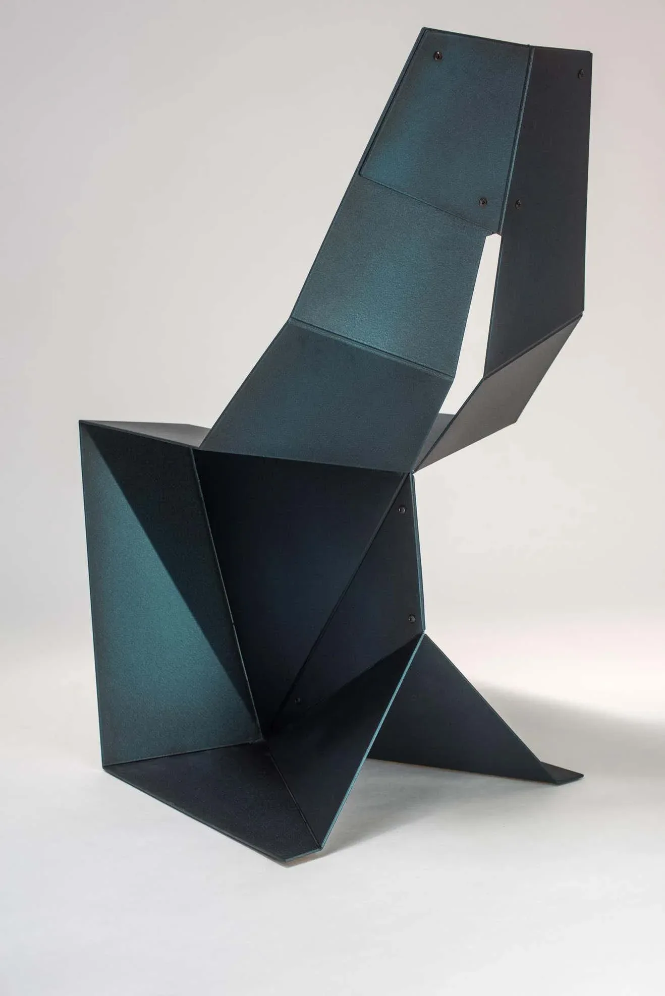 Angular geometric chair sculpture in teal and black metal with folded planes and sharp edges, photographed against white background by Arcana.