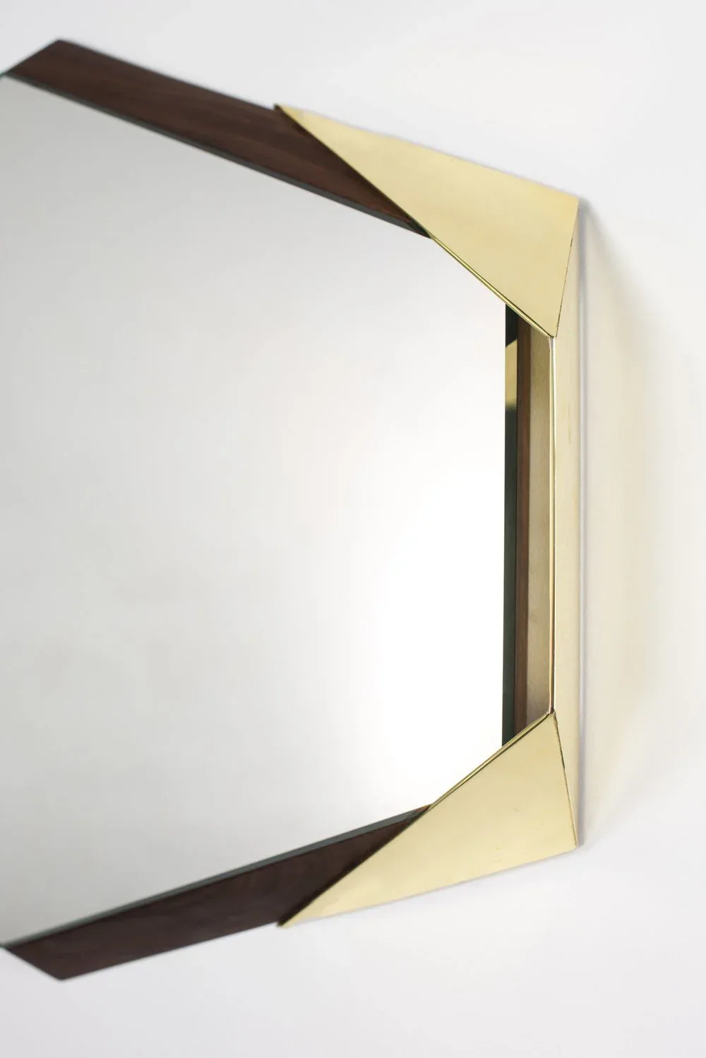 Modern mirror with geometric brass and dark wood frame detail, clean minimalist design against white wall by Arcana.