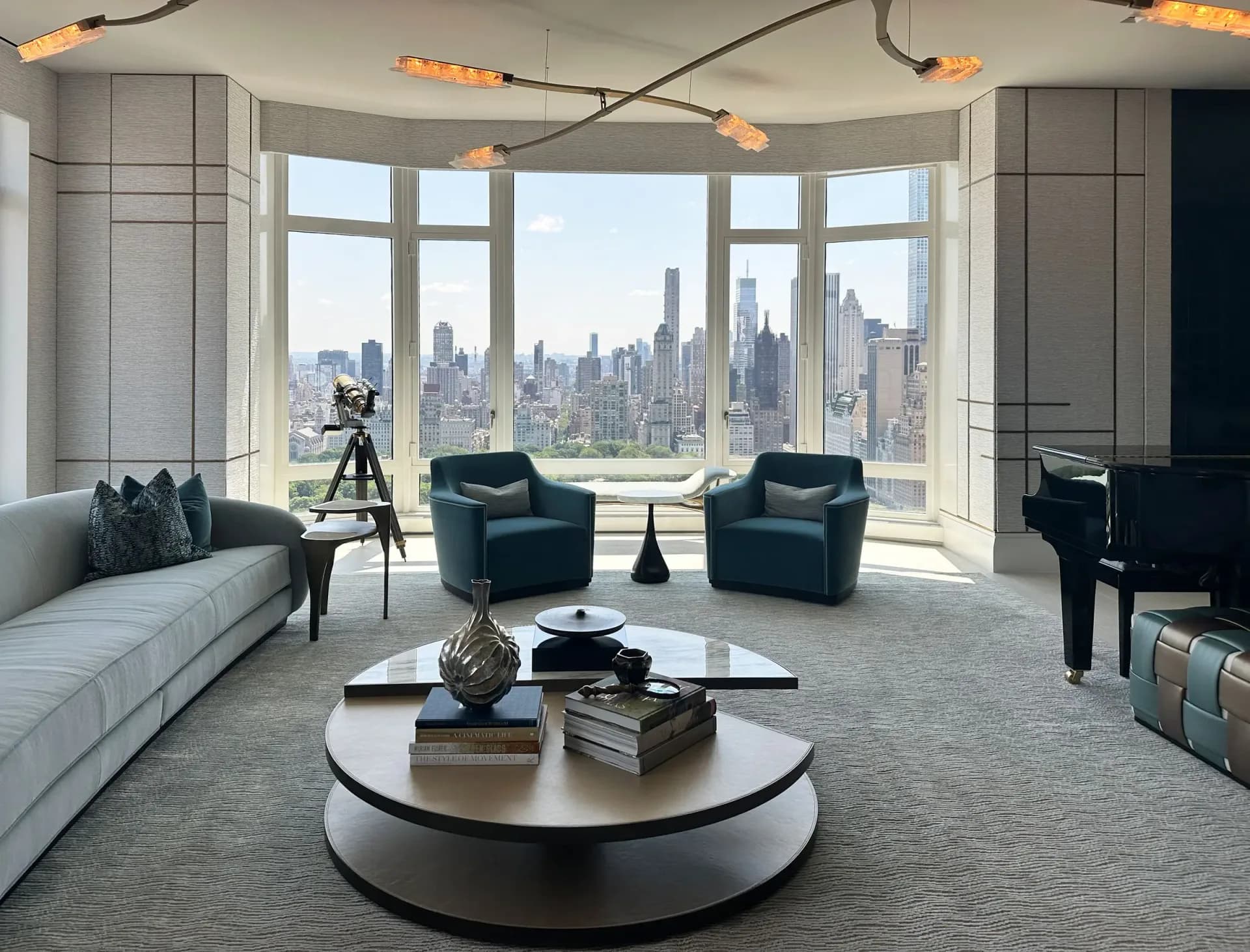Modern high-rise residential living room with curved white sofa, teal armchairs, and round marble coffee table overlooking Manhattan skyline by Archetype, LLC.