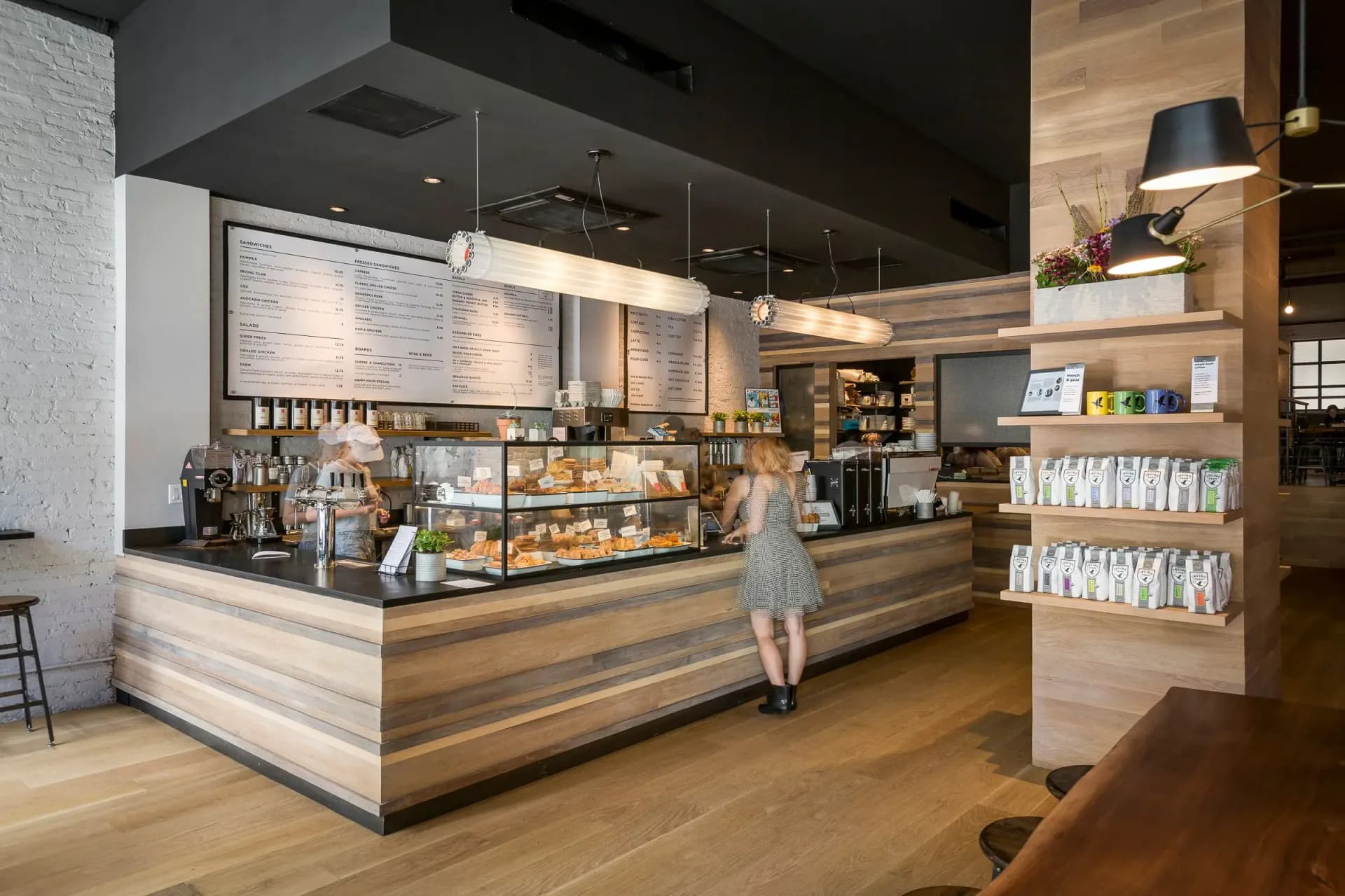 Modern café interior featuring a curved wooden counter with integrated shelving, black ceiling, wood flooring, and retail display areas by Archetype, LLC.