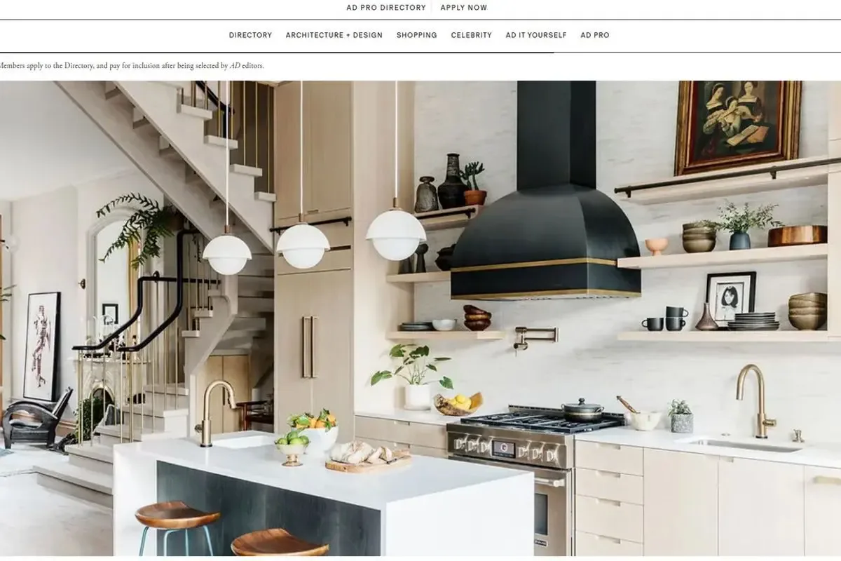 Modern kitchen with white cabinetry, black dome range hood, floating shelves, and white island with brass fixtures, designed by Archetype, LLC.