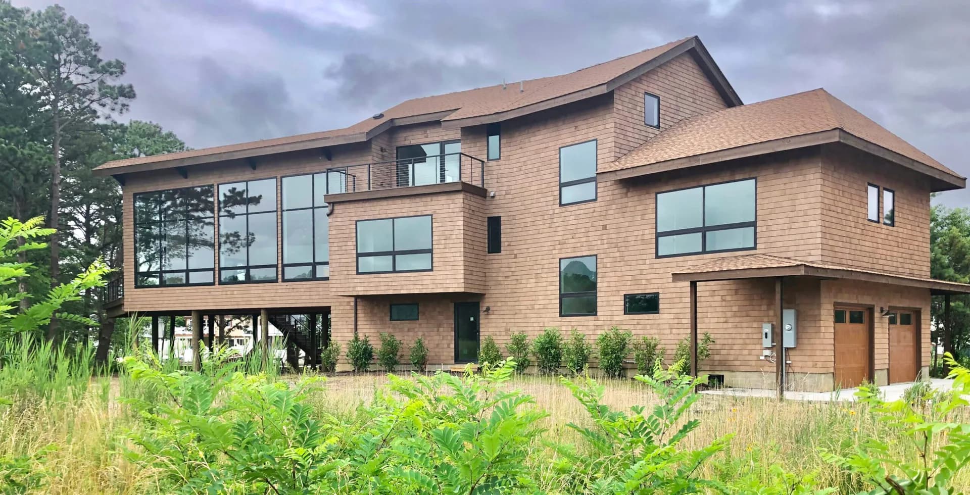 Modern brick residential building with large glazed windows, elevated on pillars, surrounded by native plantings and wildflowers by Archimuse.