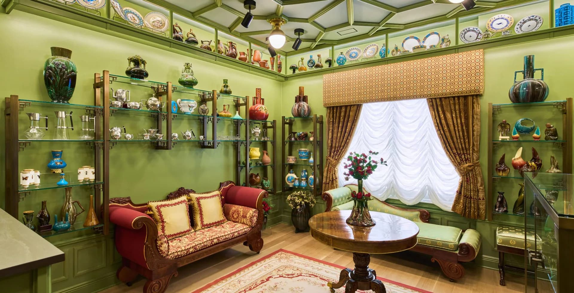 Jewel-toned green collector's room with red velvet sofa, built-in display shelving, arched glass ceiling, and ornate furnishings by Archimuse.
