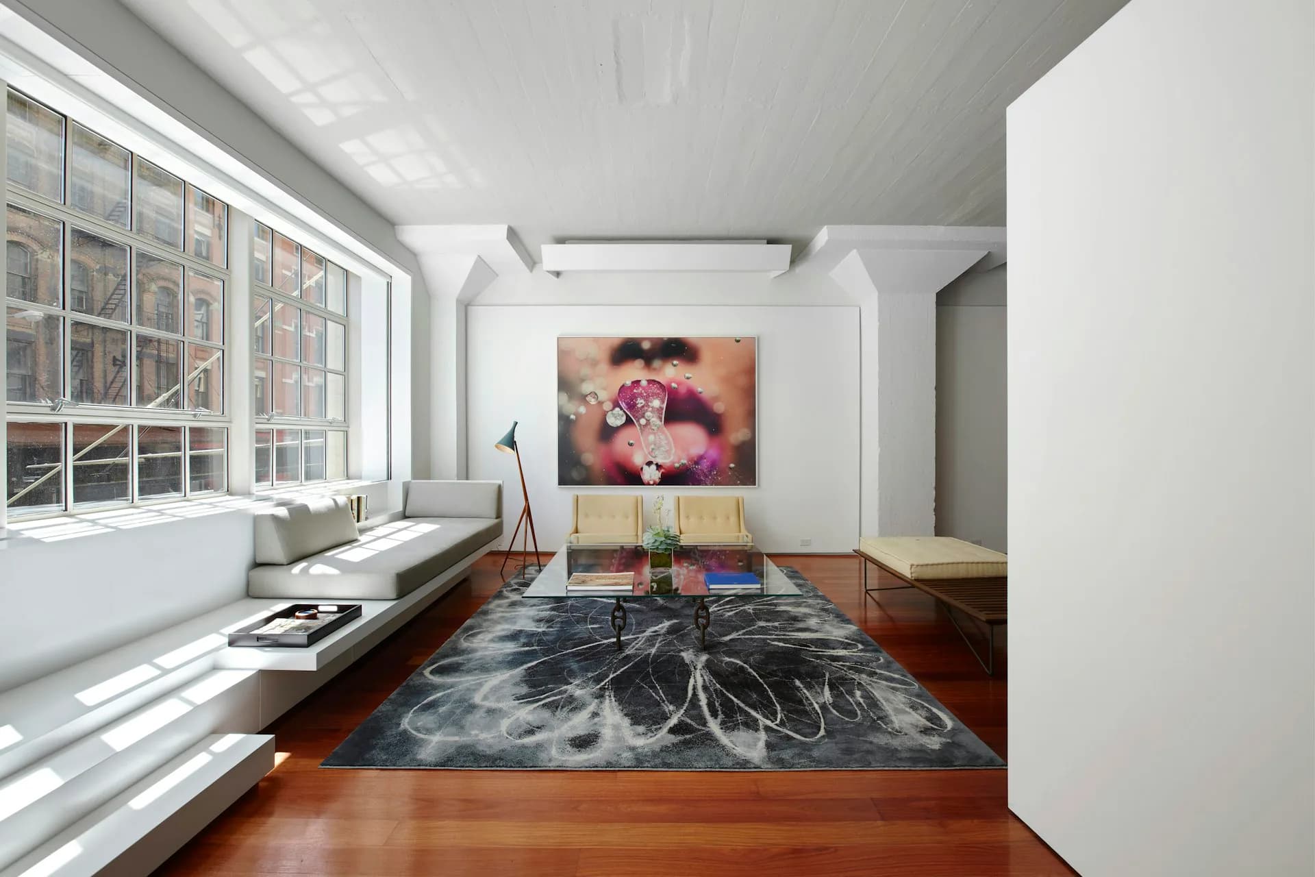 Modern minimalist loft interior with wooden floors, large windows, floating sofa, abstract artwork, and geometric black area rug by Architecture in Formation.