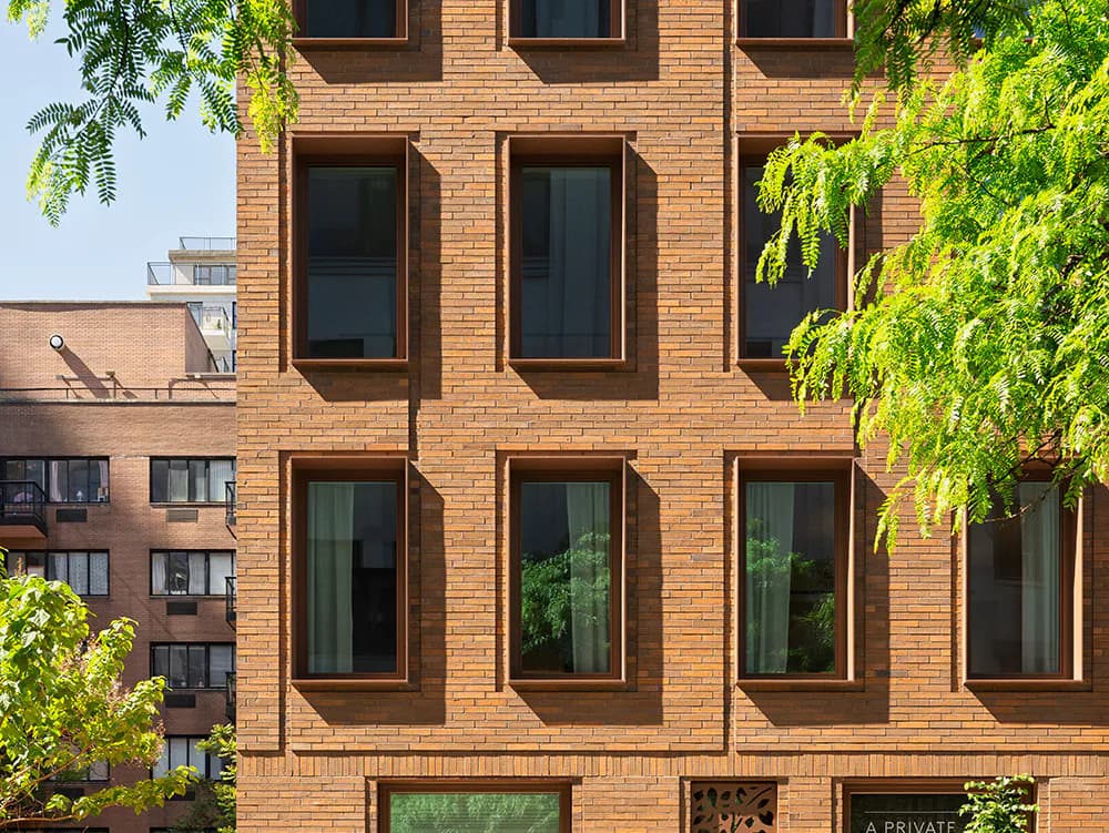 Brick residential building facade with stacked rectangular windows, climbing ivy, and neighboring structures visible, designed by ARCHITECTURE OUTFIT PLLC.