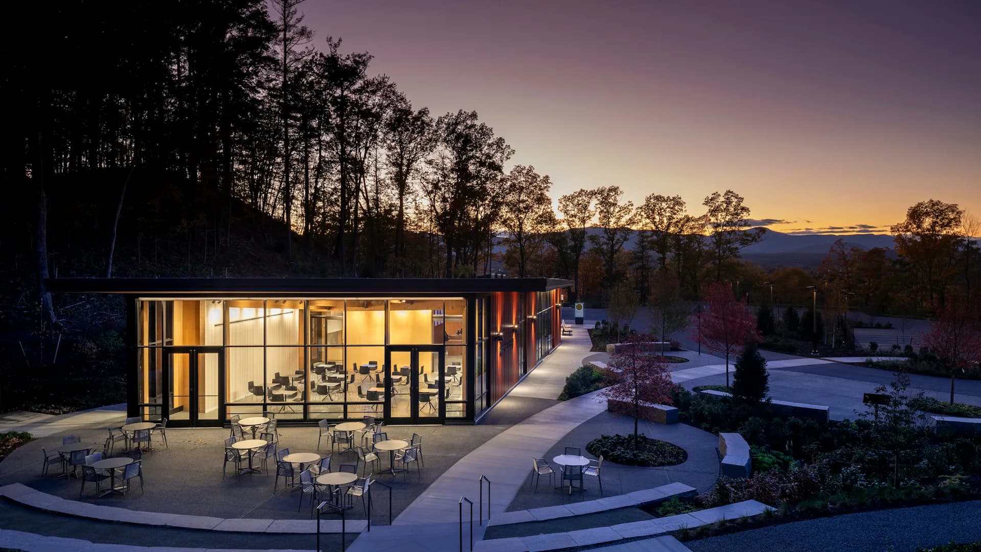 Modern glass pavilion illuminated at dusk with wooden interior, surrounded by snow and evergreen trees, designed by Architecture Research Office.