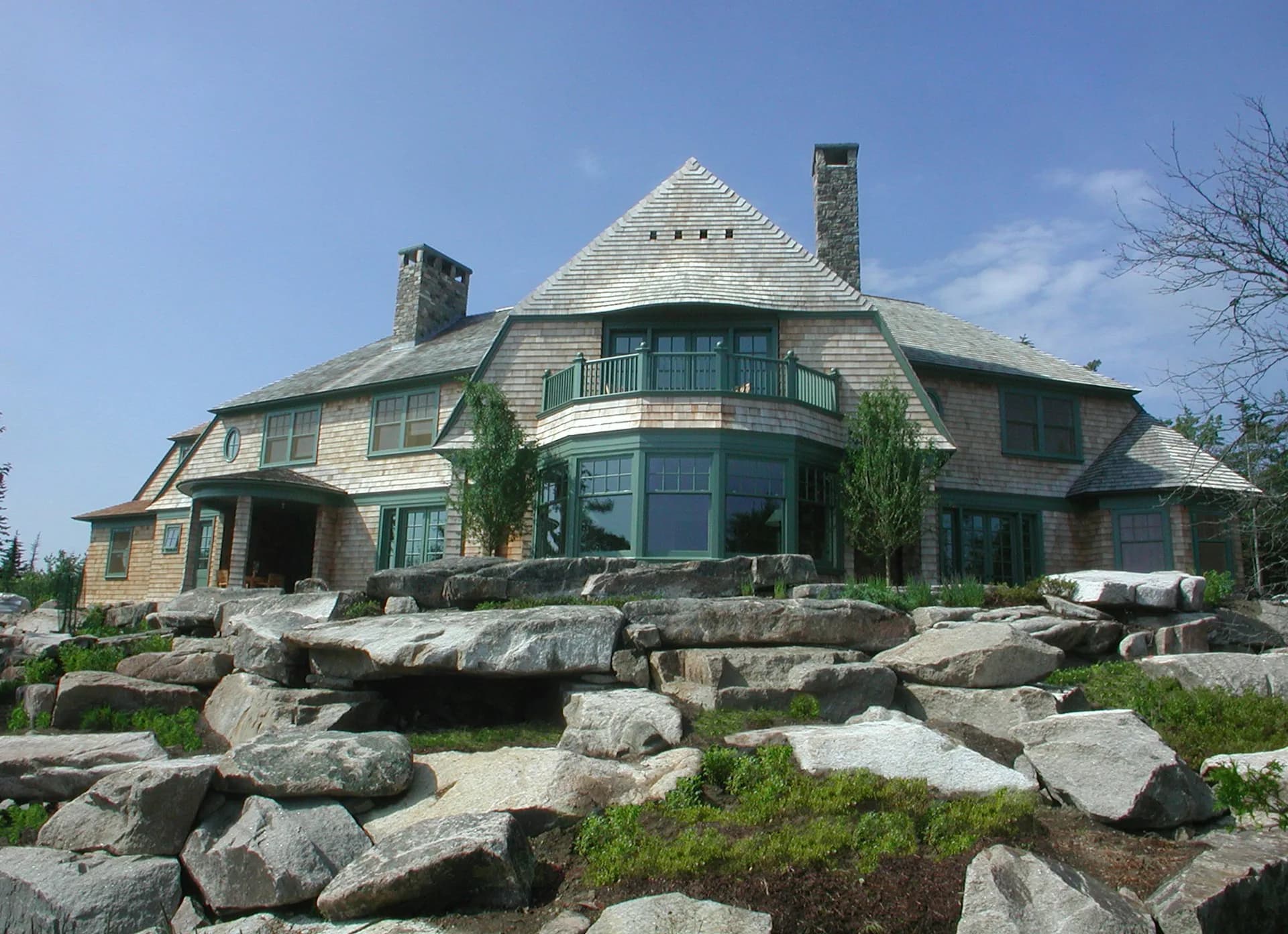 Modern residential estate with stone and shingle exterior, curved architectural forms, and large glass windows situated on rocky landscape designed by Armand LeGardeur Architect.