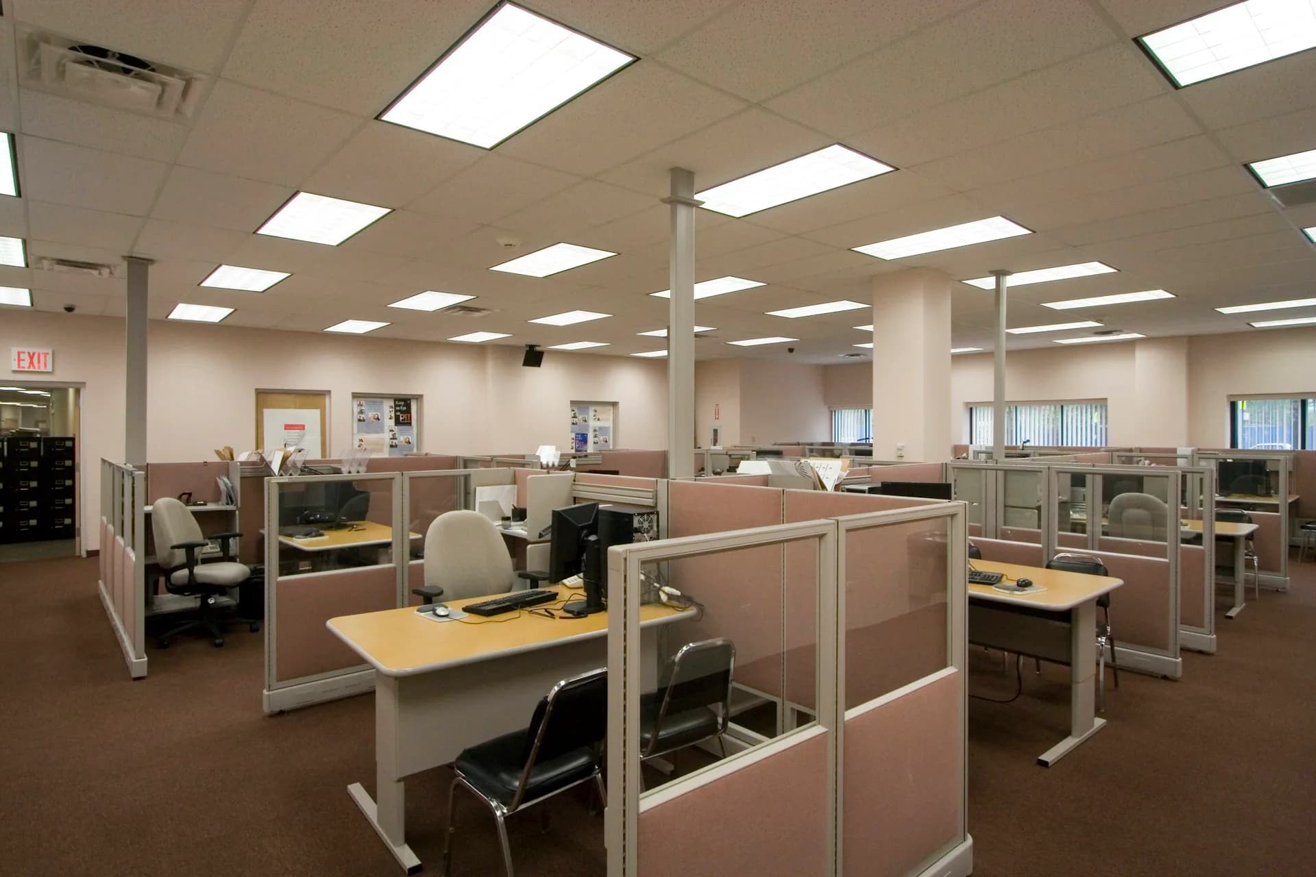 Open-plan office space with modular workstations, beige partition walls, and fluorescent ceiling panels in a neutral color palette, designed by Arpad Baksa Architect, P.C.
