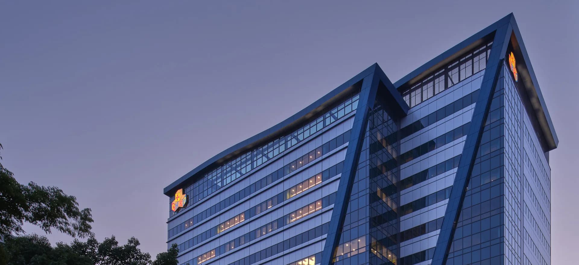 Modern multi-story office building with blue-tinted glass façade and horizontal striping, photographed at dusk against a purple sky by Array Architects.