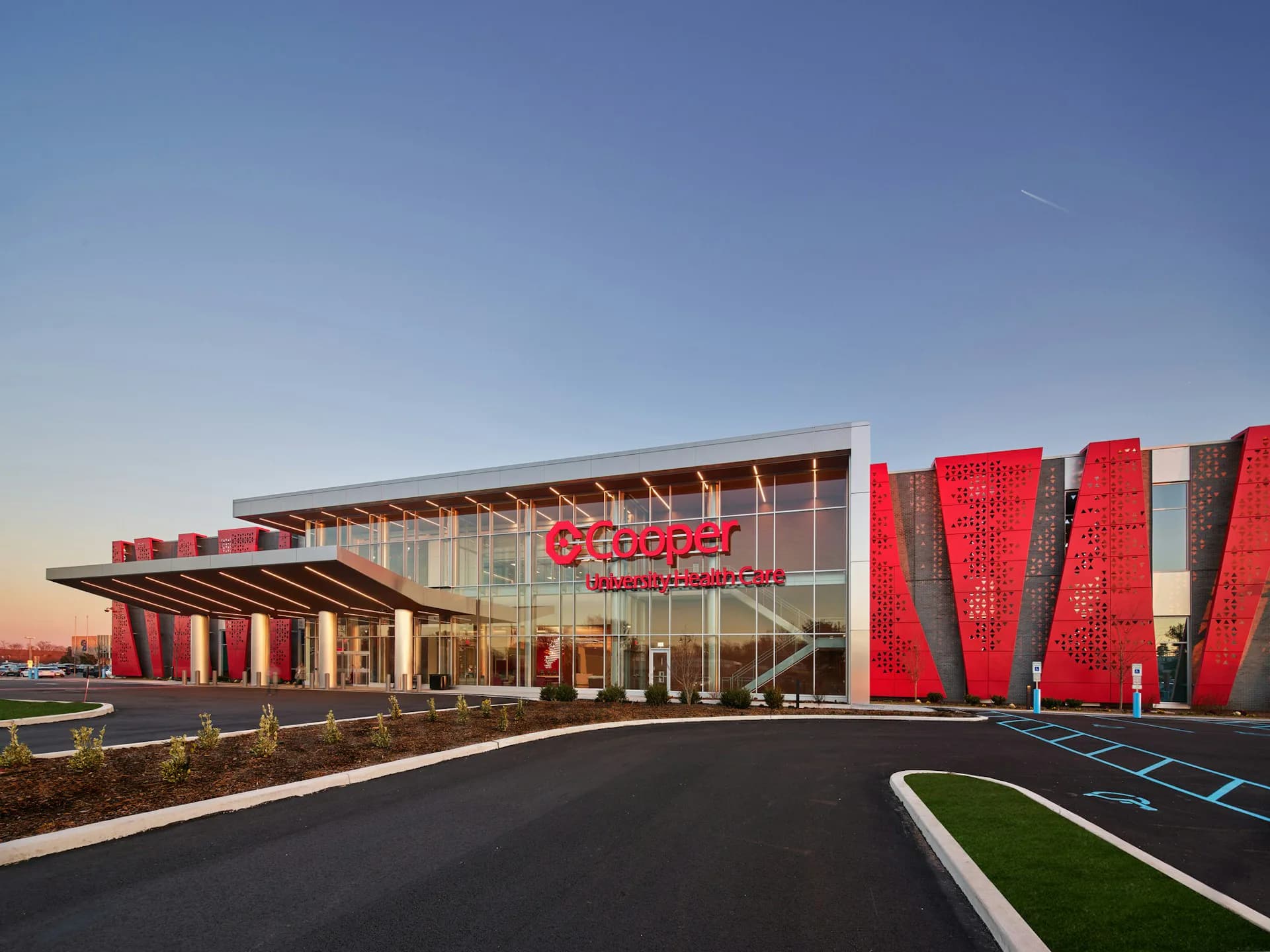 Modern institutional building with glass and metal facade, featuring striking red sculptural vertical elements on exterior, photographed at dusk by Array Architects.