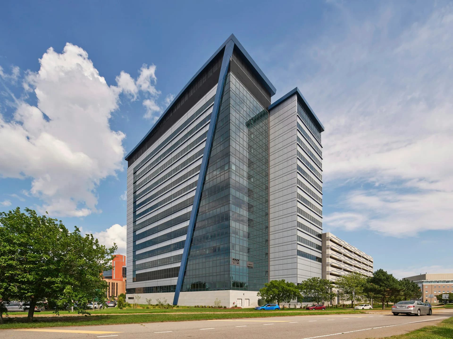 Modern glass and metal office tower with angular rooflines and horizontal striping, set in a landscaped plaza by Array Architects.