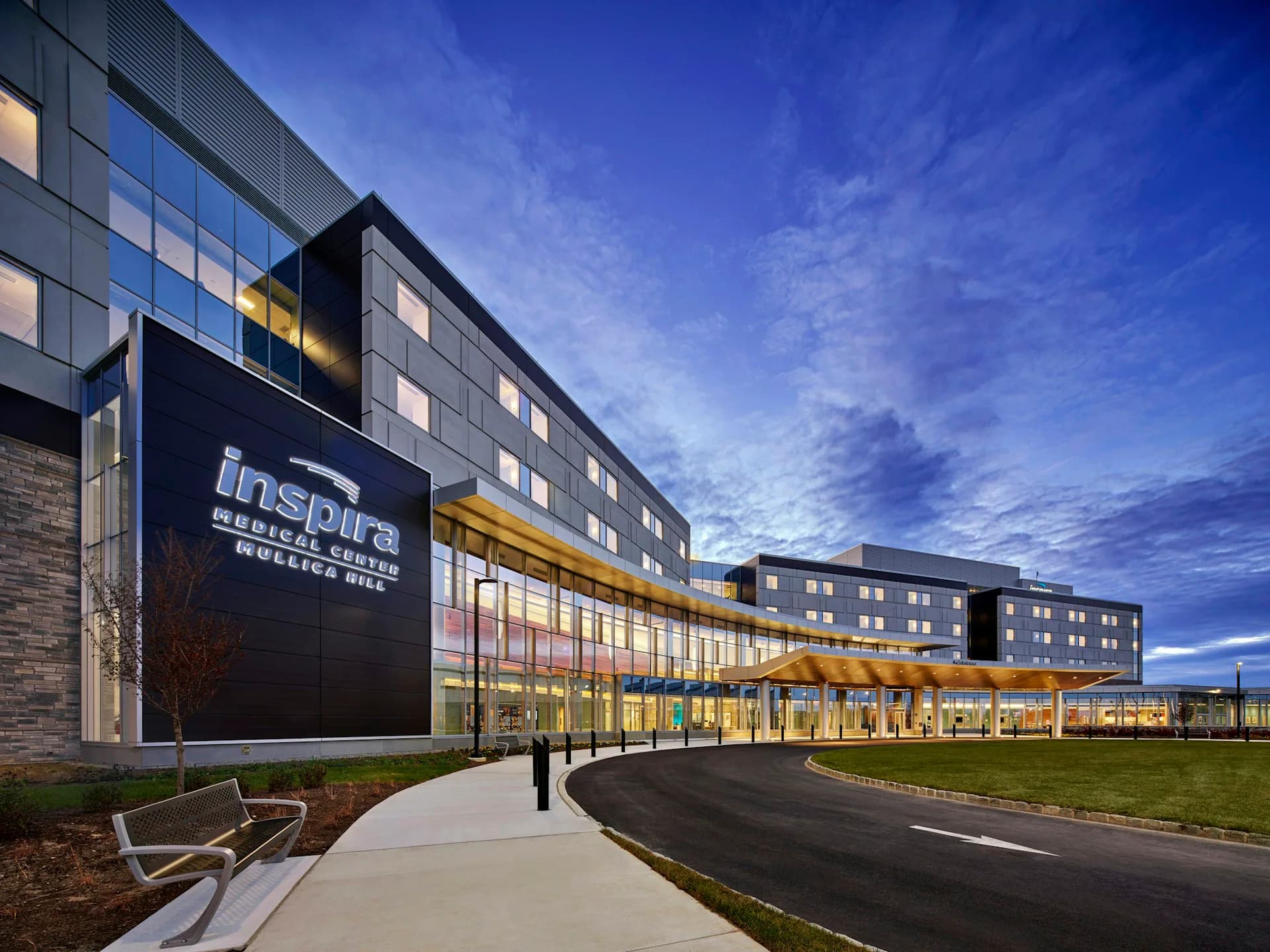 Modern institutional building with dark and light facade panels, illuminated ground-level glazing, and open plaza grounds photographed at dusk by Array Architects.