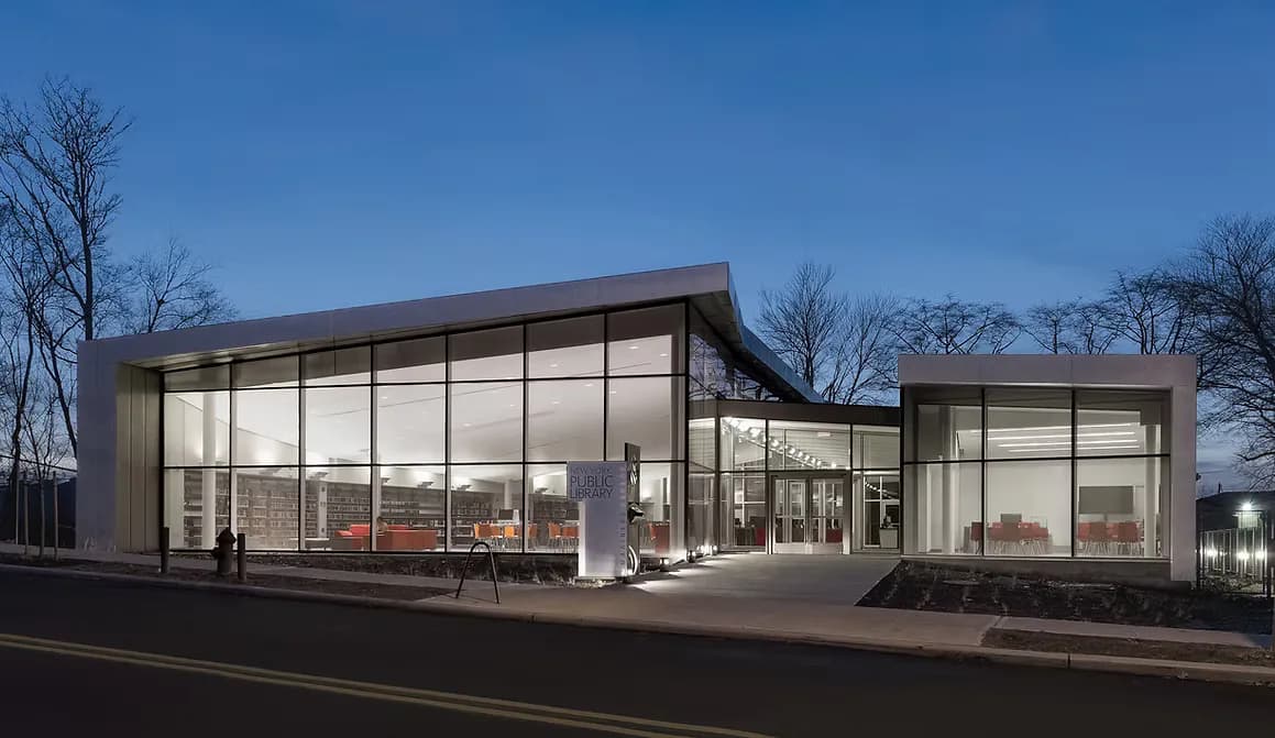 Modern commercial building with extensive glazing, concrete frame, and minimalist design lit at dusk by Atelier Pagnamenta Torriani.
