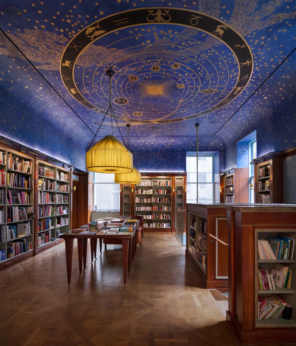 Luxurious library interior with zodiac-patterned ceiling, wood paneling, golden pendant lights, and bookshelves by Atelier Premiere.